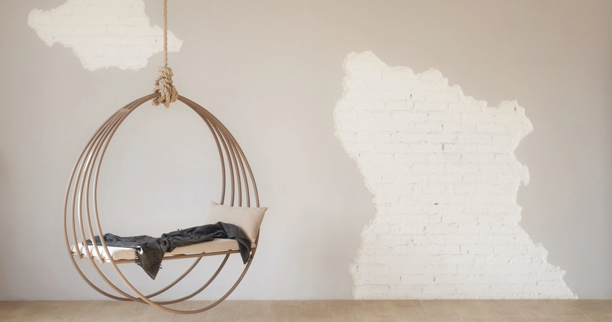 Indoor swing chair with beige cushion and black clothing draped on it, hanging from a ceiling with a knotted rope, against a light-colored wall with a painted brick silhouette of France.