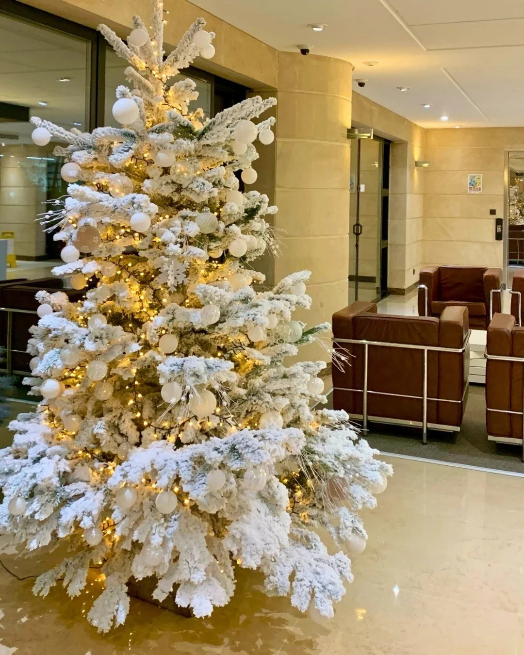 Scénographie de Noël : sapin blanc floqué et illuminé dans le hall d'un hôtel