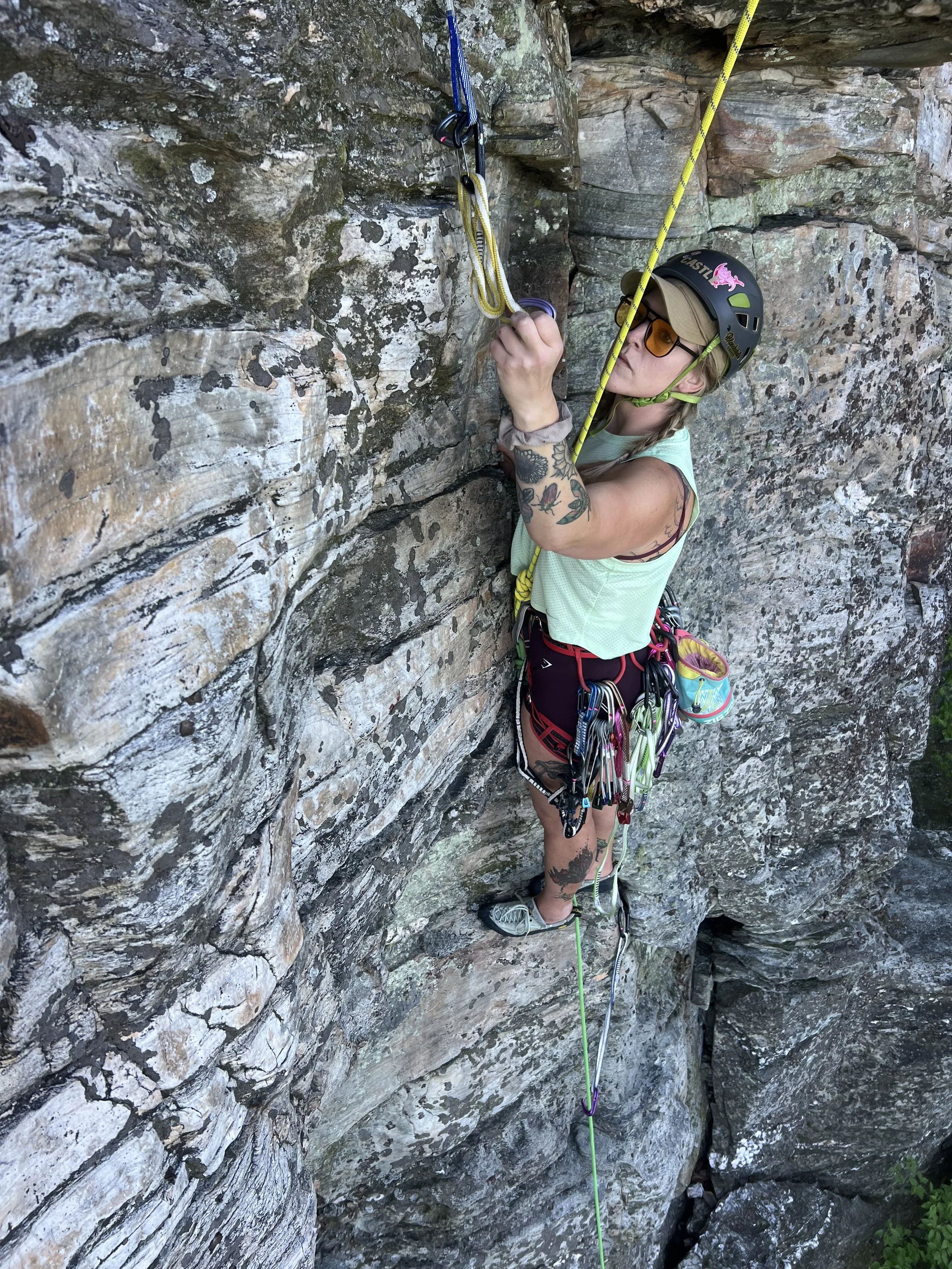 A rock climber learning lead climbing skills on a rocky cliff face during a climbing activity.