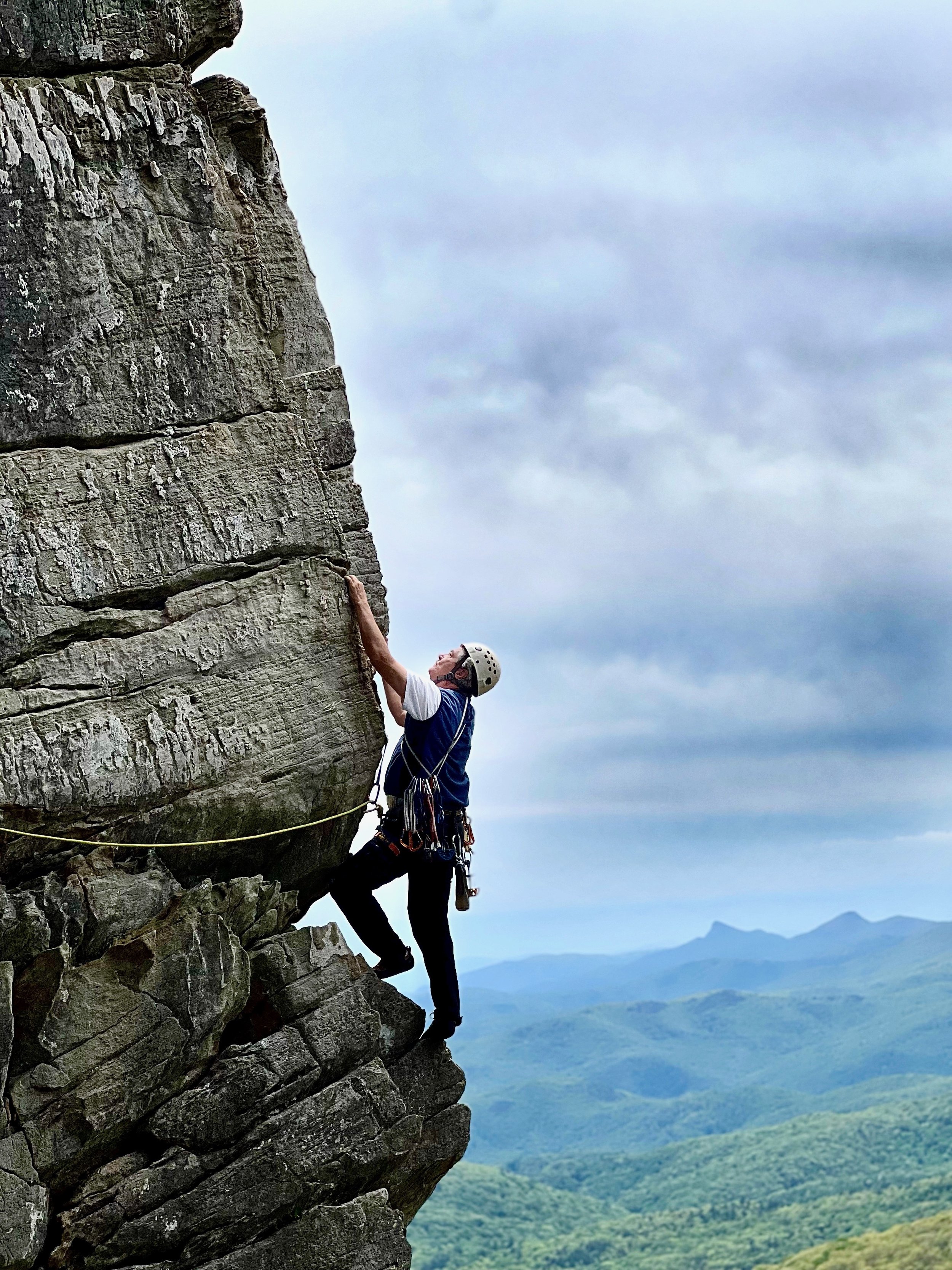 A person wearing a helmet and climbing gear ascending a climb called "Edge Of a Dream" at Ship Rock, Located on the Blue Ridge Parkway near Boone North Carolina