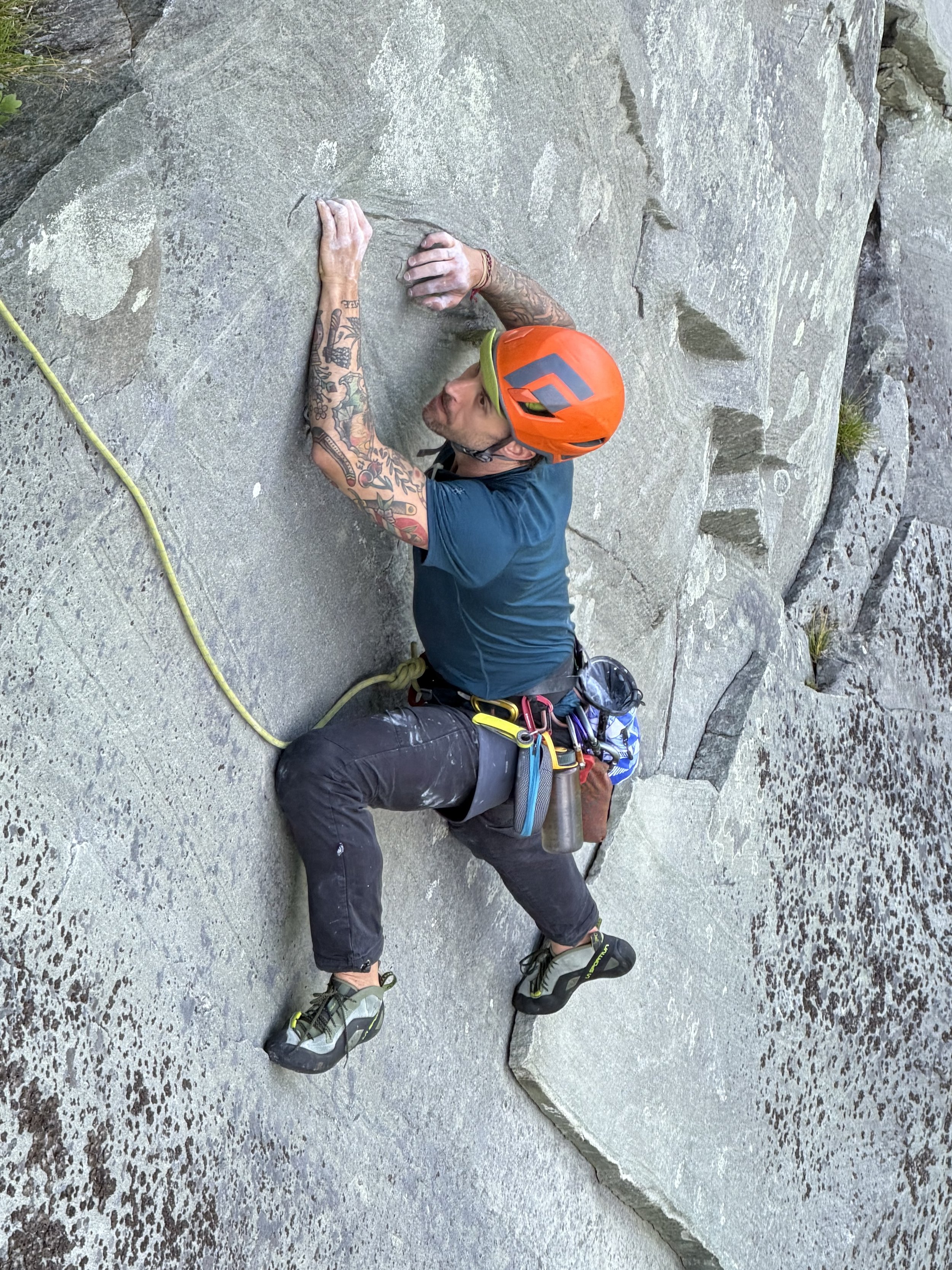 A man with tattooed arms wearing a helmet and climbing gear is climbing at Ship Rock Located on the Blue Ridge Parkway.