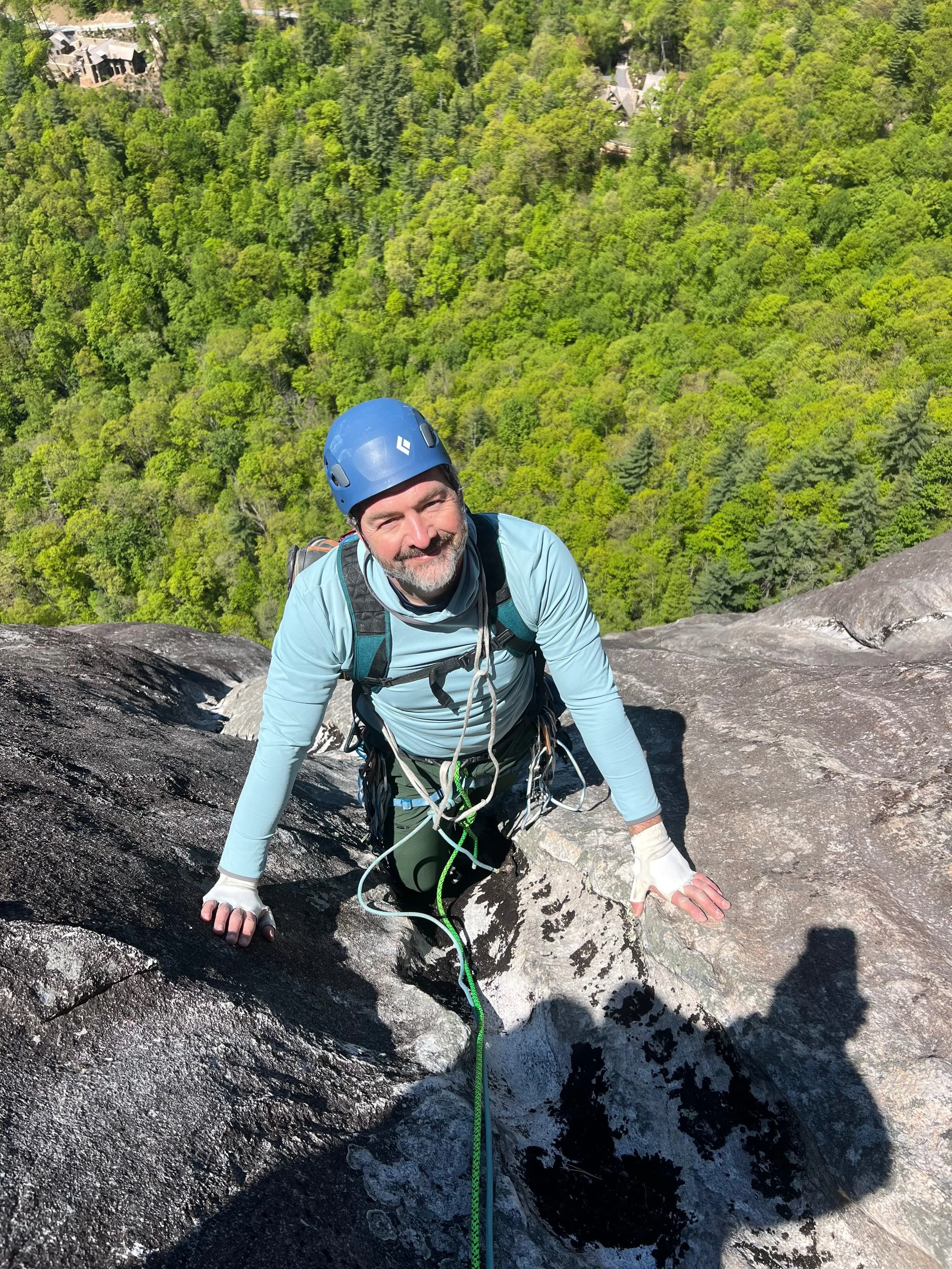 A rock climber with  ropes and equipment standing in the middle of a rock face called Laurel Knob.