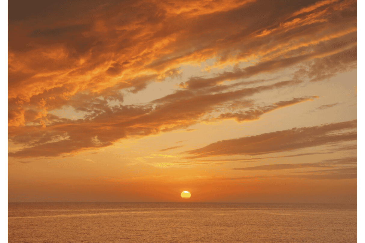 Sunset over the ocean with orange and yellow clouds in the sky.