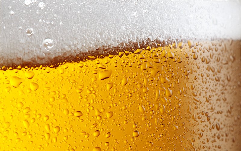 Close-up of a glass of beer with condensation droplets on the outside and foam on top.