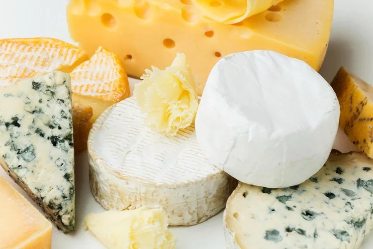 Various cheeses including a wedge of Swiss, a wheel of Brie, a chunk of Gouda, and a blue cheese slice.
