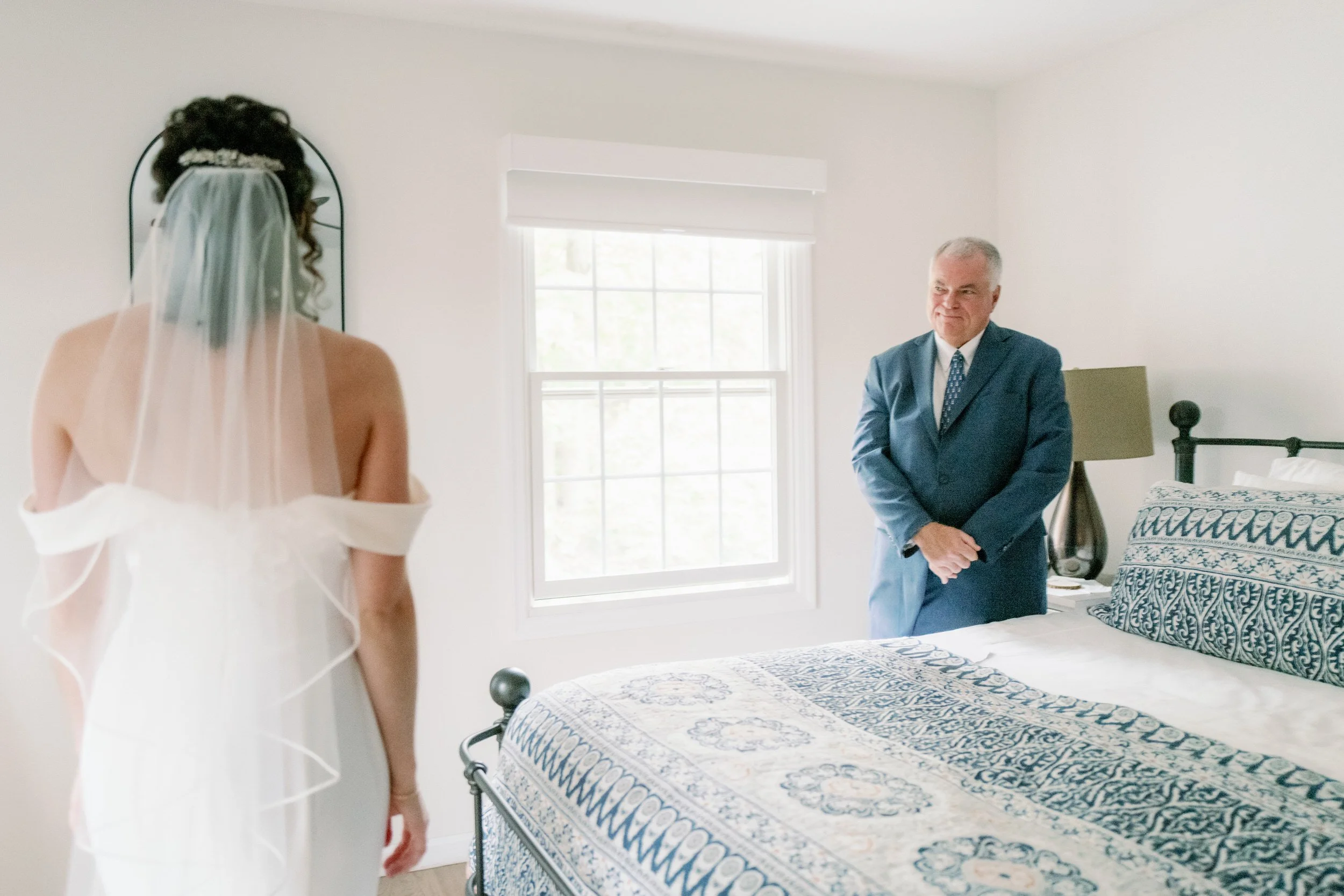 A person in a wedding dress standing in a bedroom during a first look with their parent 