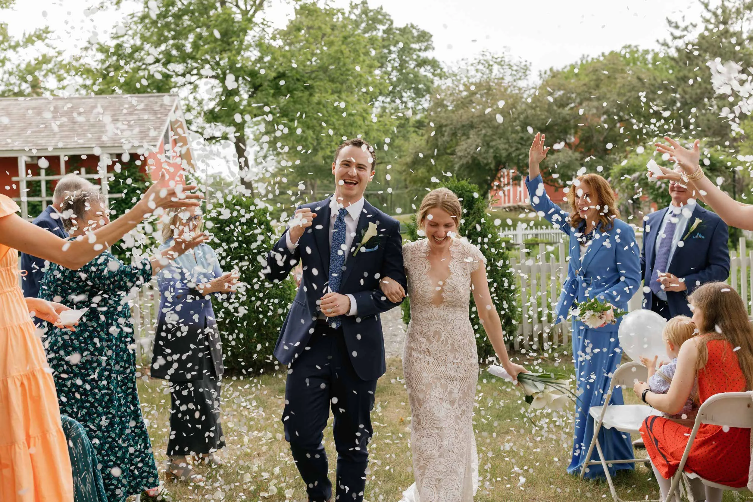 Newlyweds laughing as guests throw flower petals around them