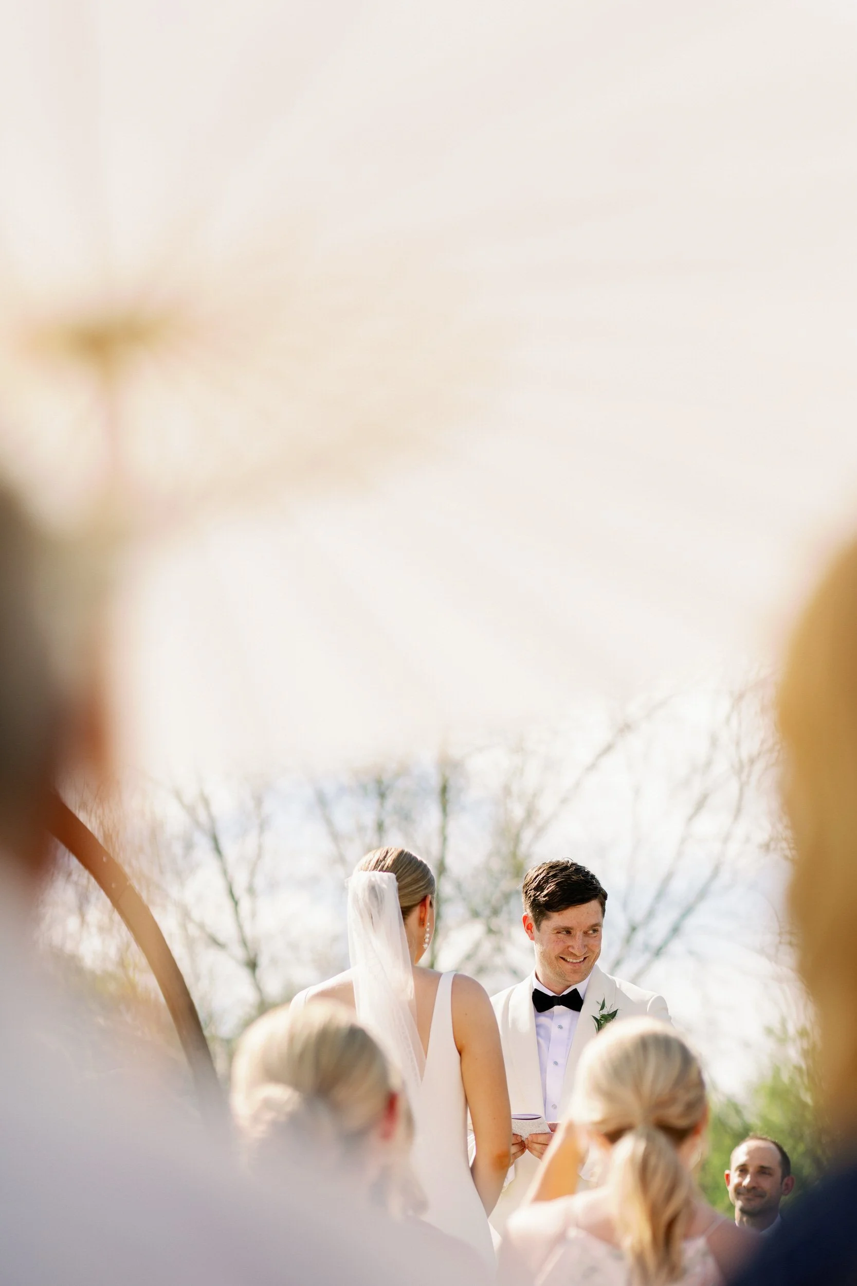 A newlywed couple standing up at their wedding ceremony seen through a gap in their wedding guests' heads 
