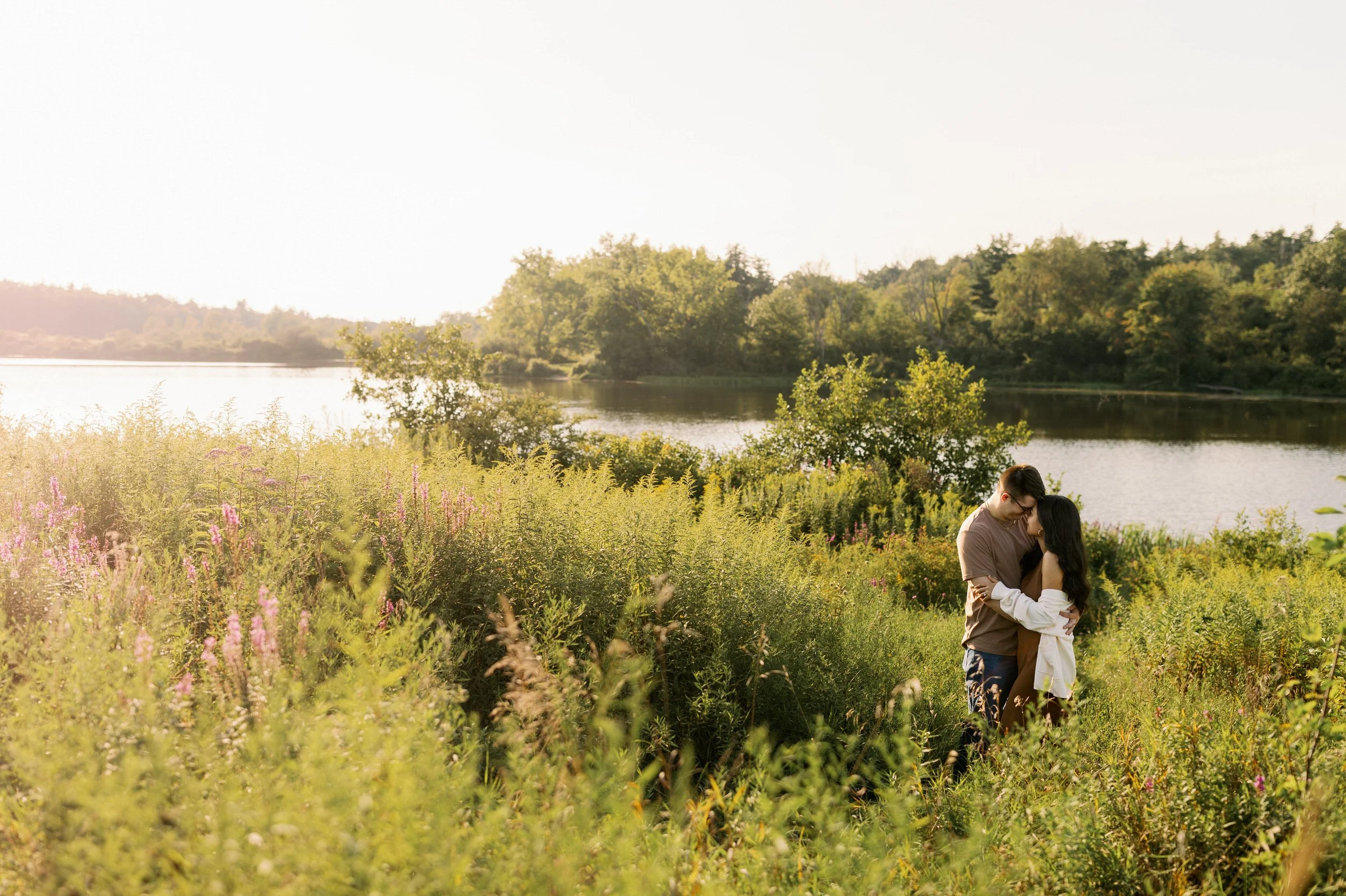 A couple standing forehead to forehead on the grassy banks of a river
