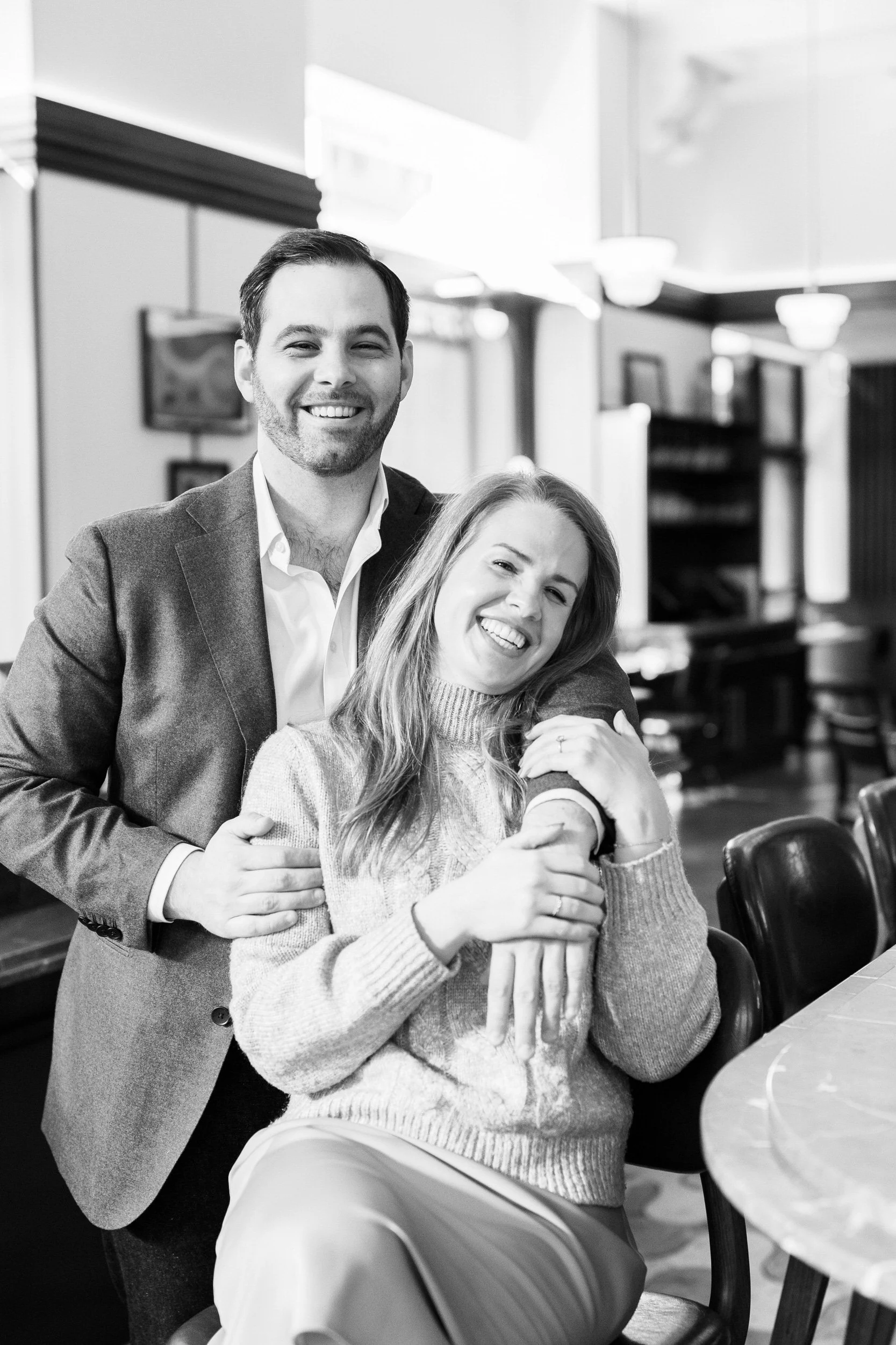 A person sitting on a stool leaning back into their partner as they both smile 