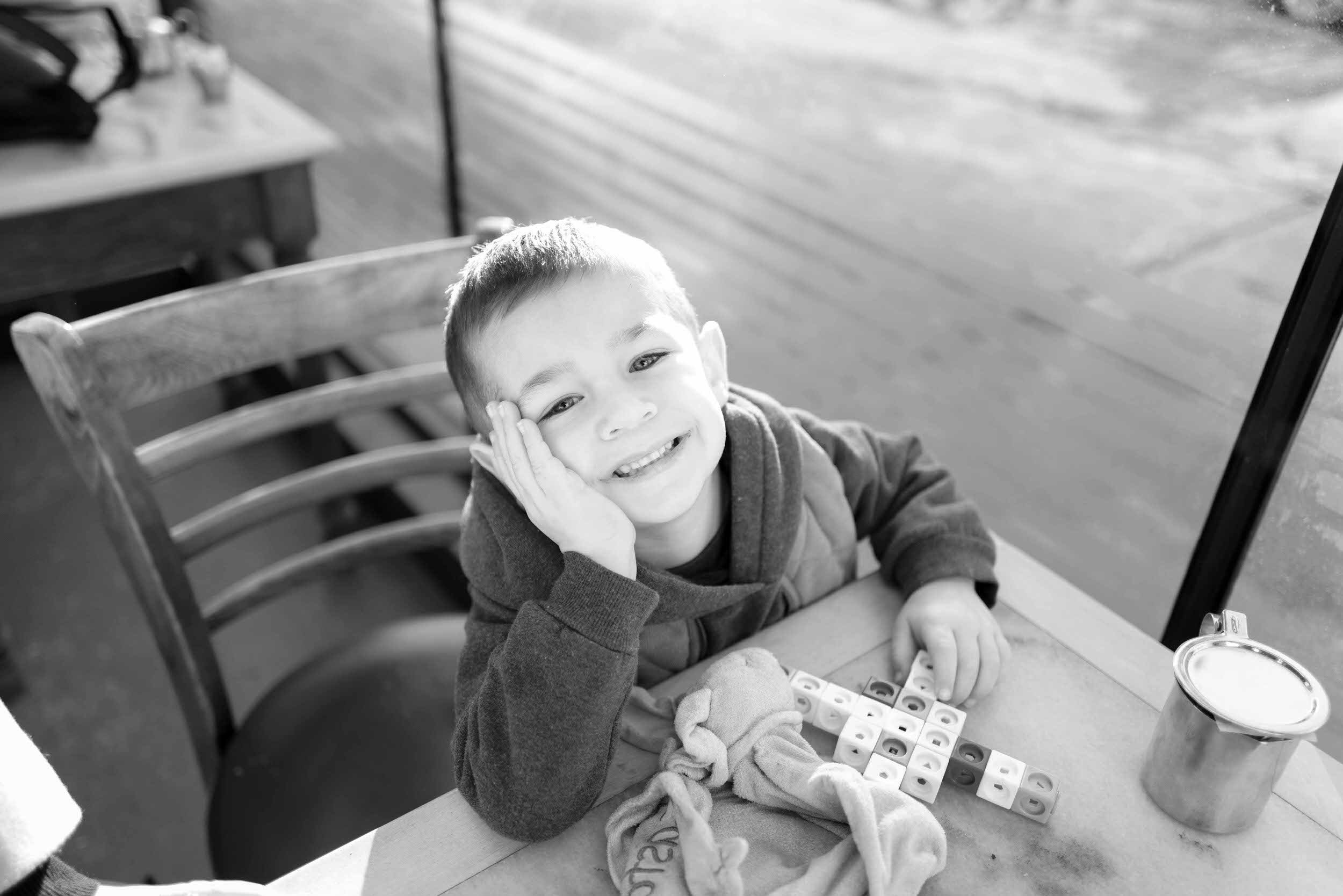 A small child sitting at a table smiling with their head rested in their hand