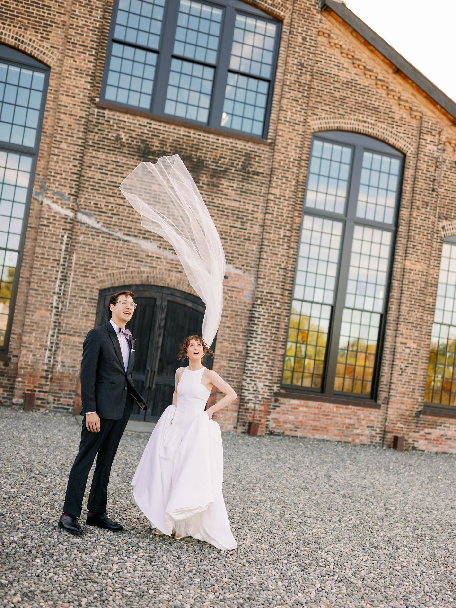  Newlyweds smiling and looking up at a veil flowing in the wind 