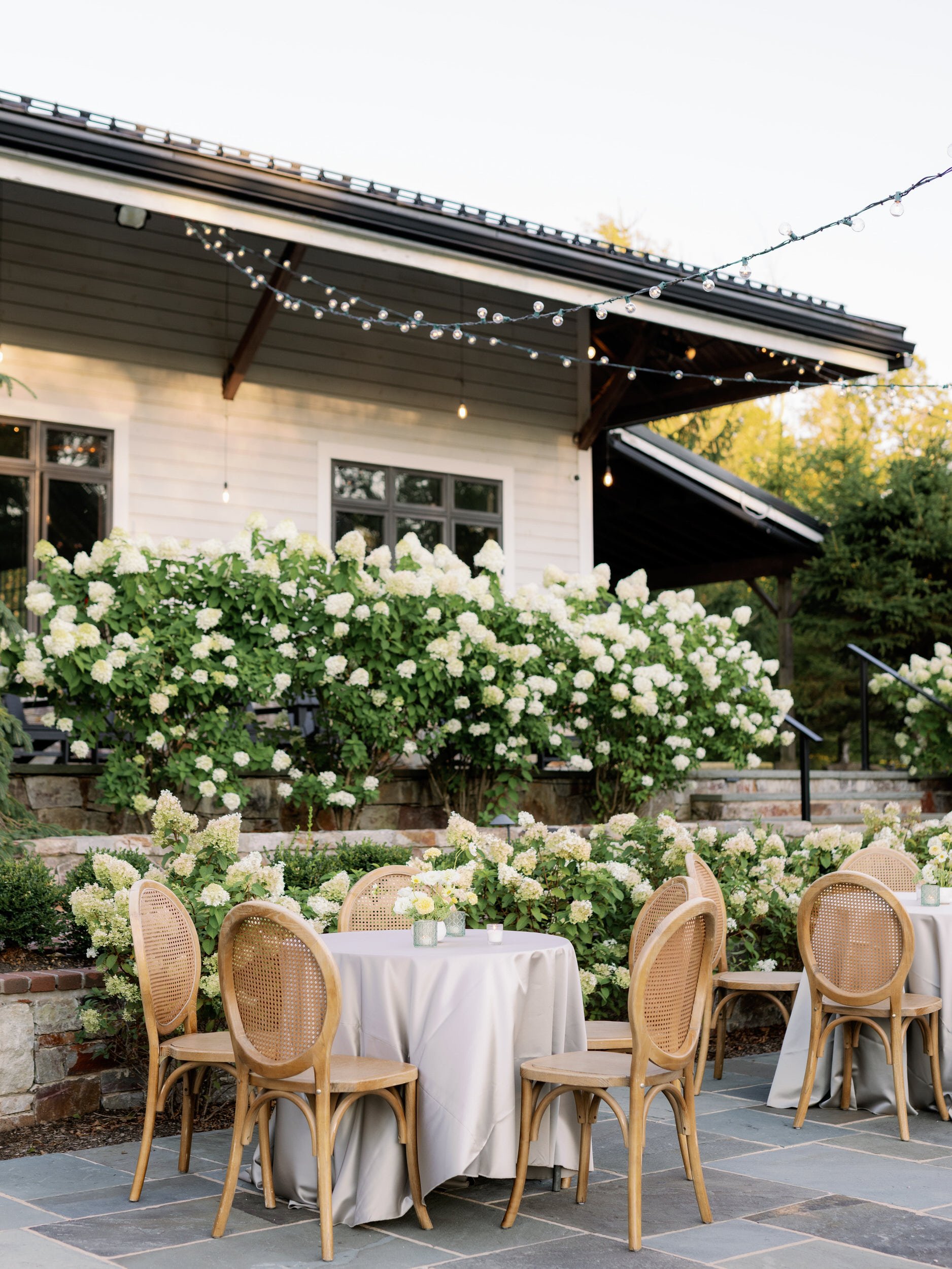  Small tables and chairs set up on a patio with string lights overhead 