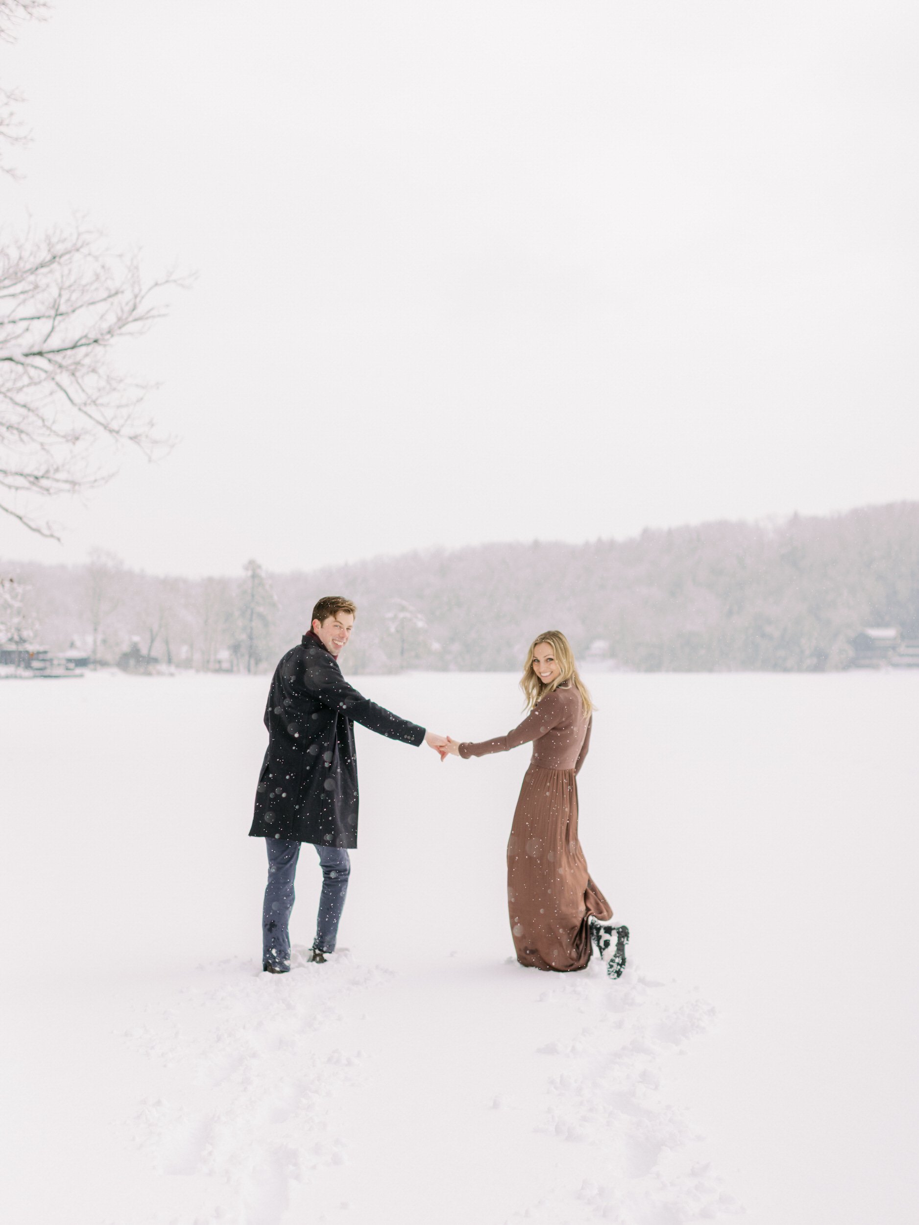 A couple holding hands and looking back over their shoulders as they walk in the snow 