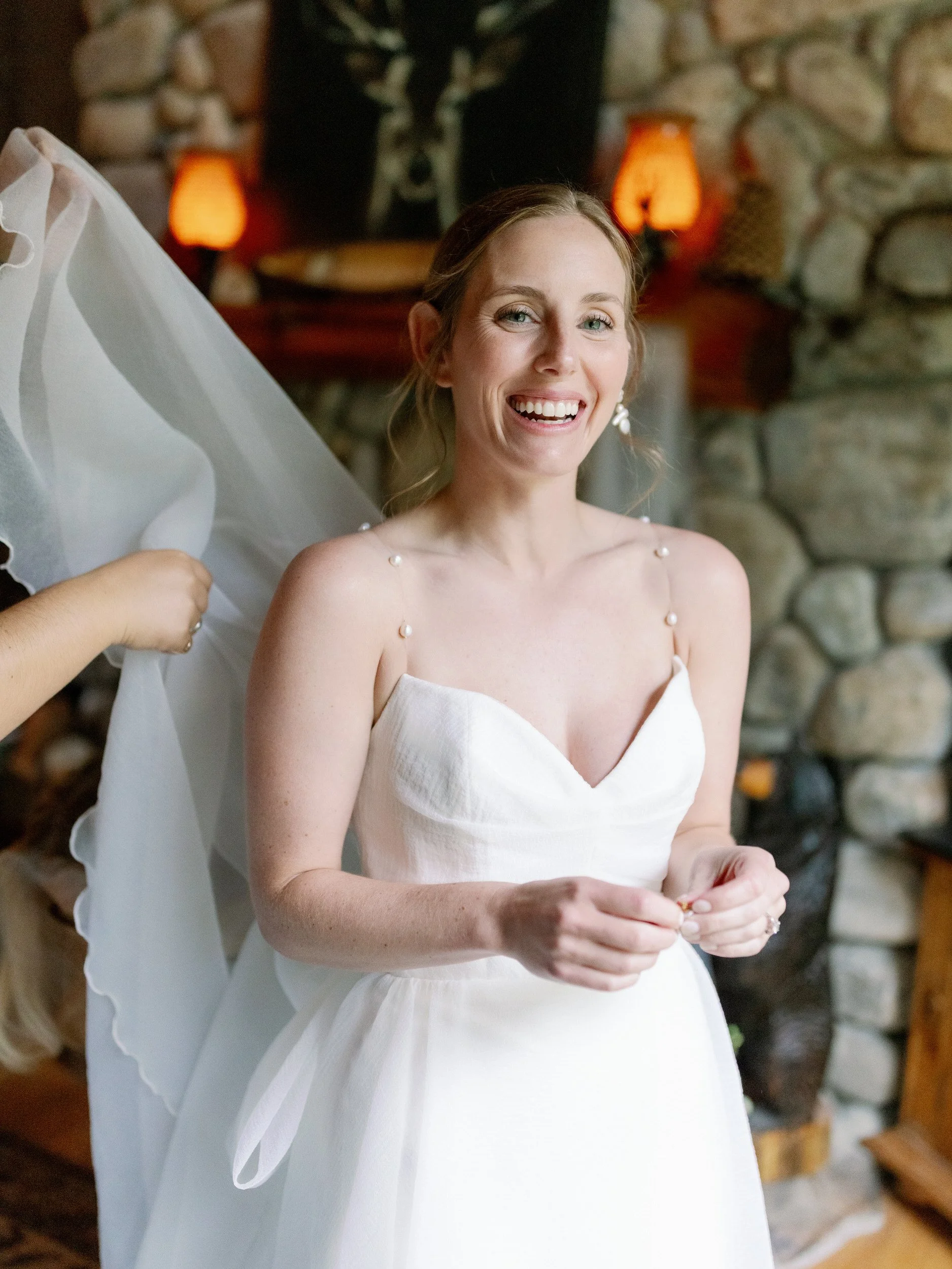 A person in a wedding dress smiling as someone adjusts the back 