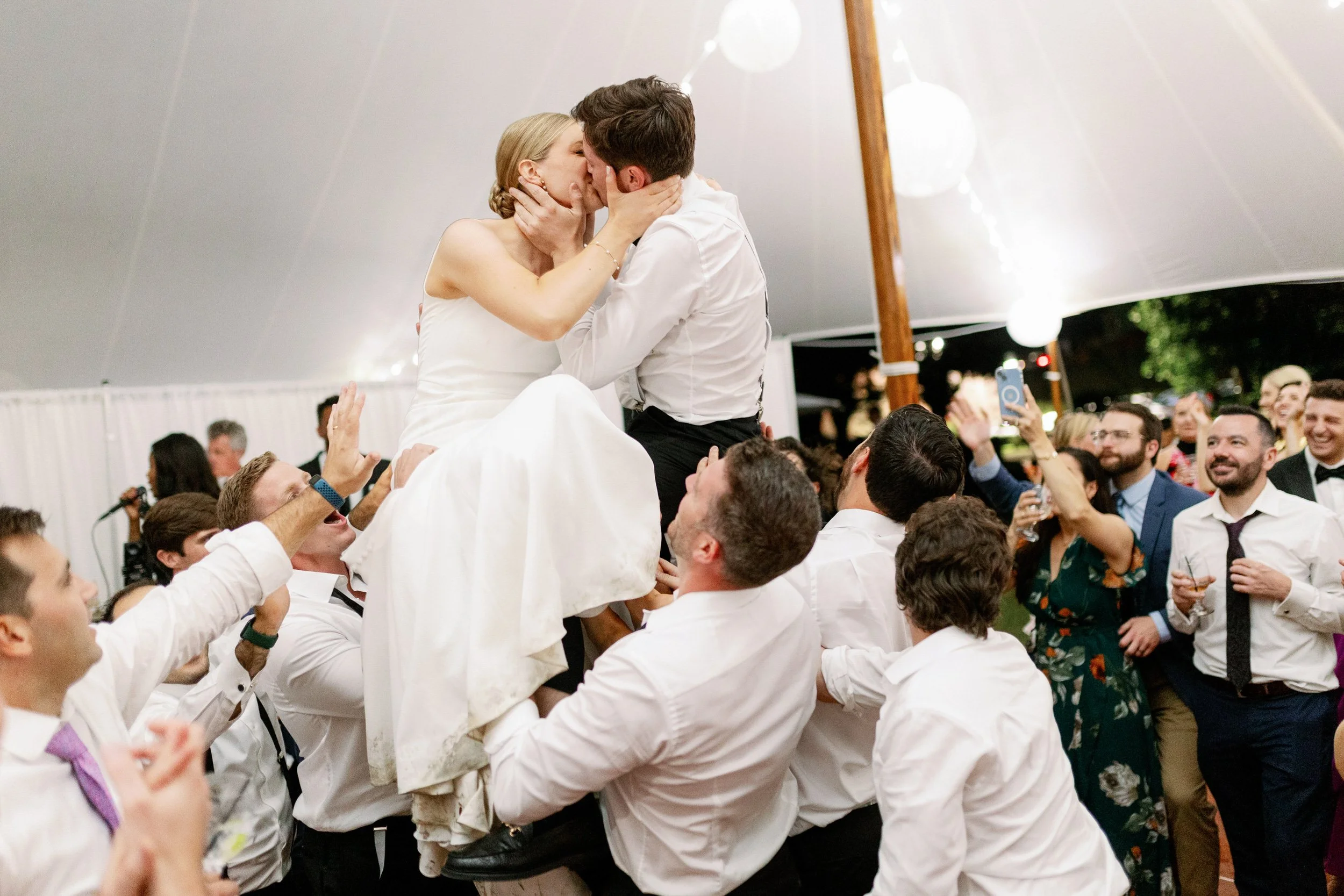 A newlywed couple kissing as they are help up in the air by the wedding guests 