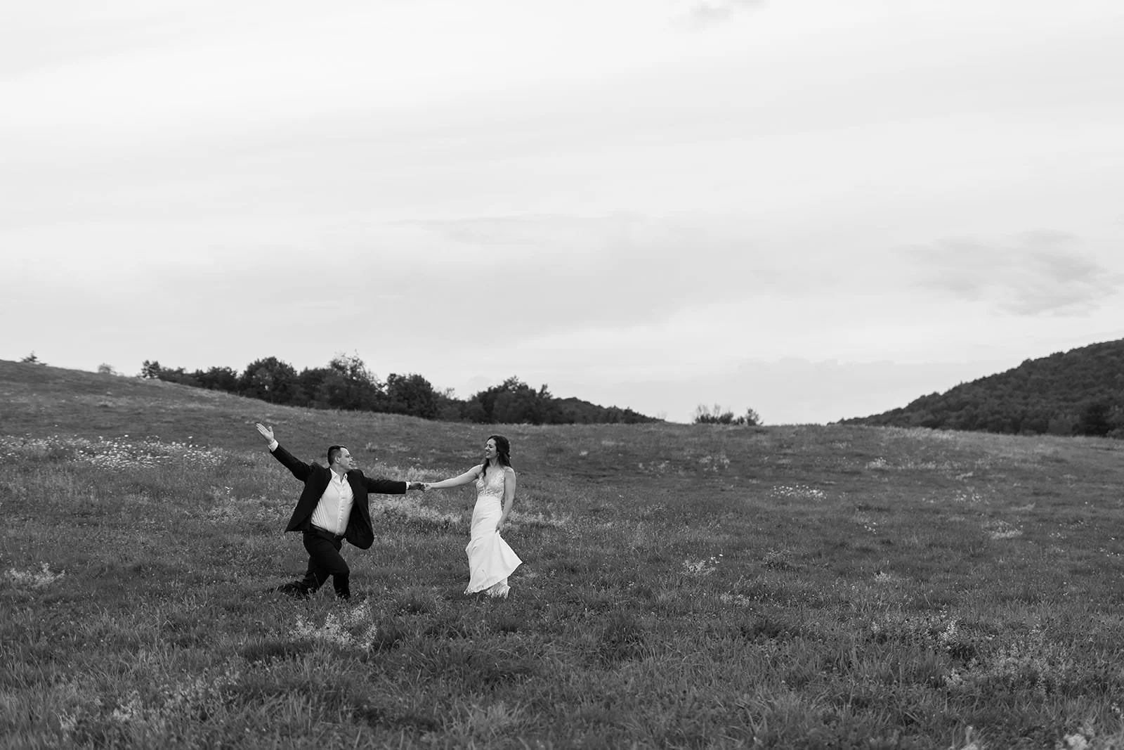 Newlyweds holding hands and walking in a field as one of them has their other hand outstretched 