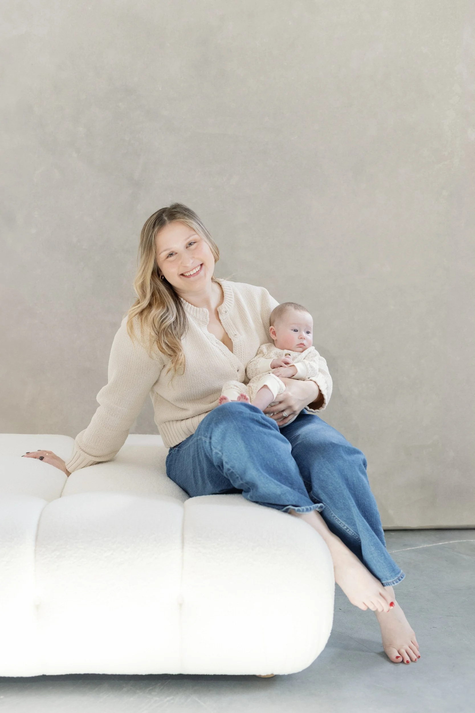 A parent sitting on a white couch while holding their newborn 
