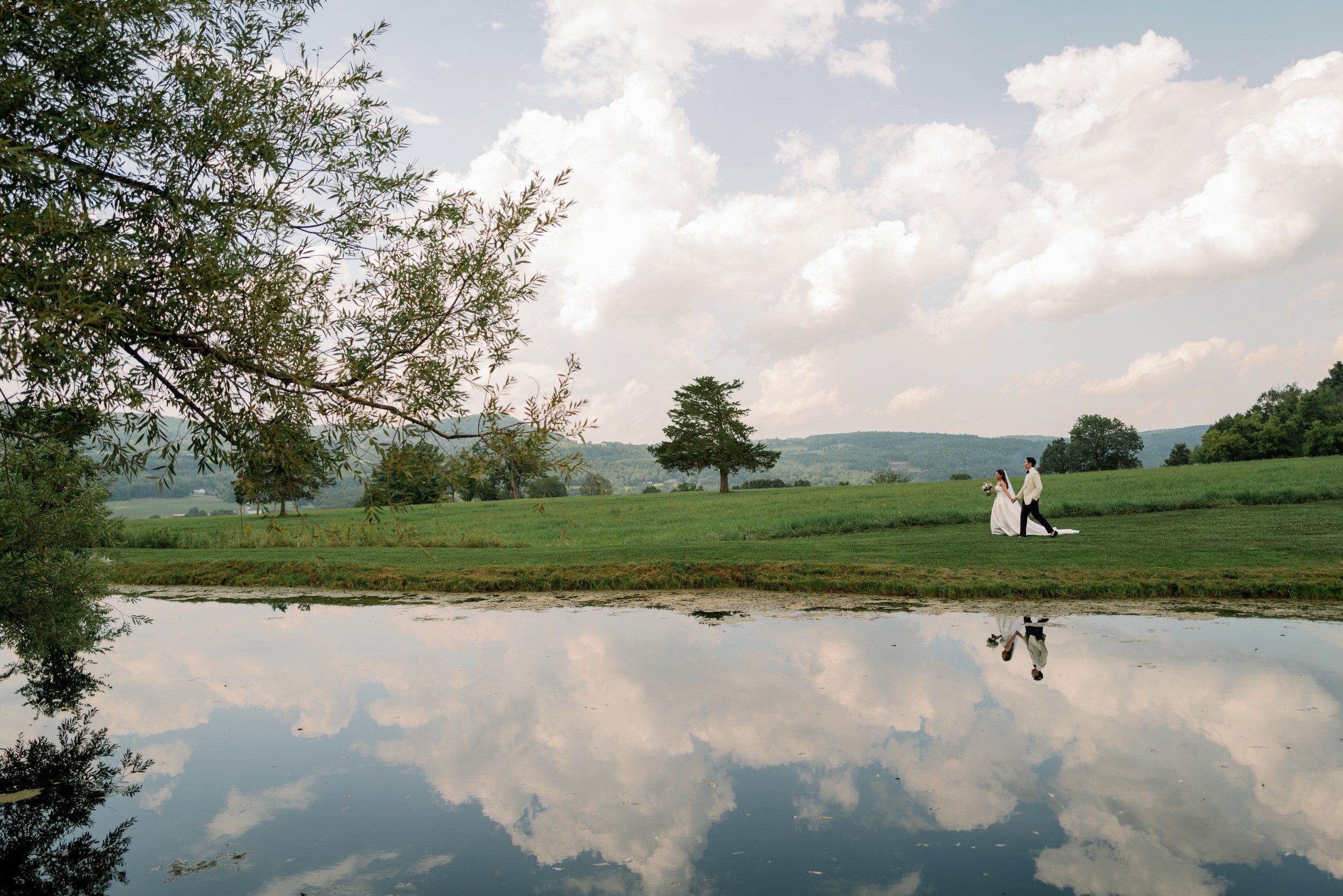 Newlyweds walking along a field next to a lake 