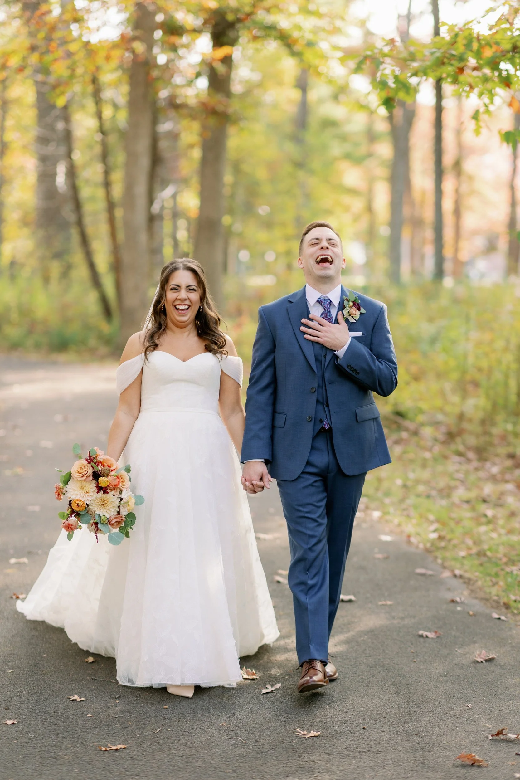 a newlywed couple holding hands and walking along a road while they laugh 