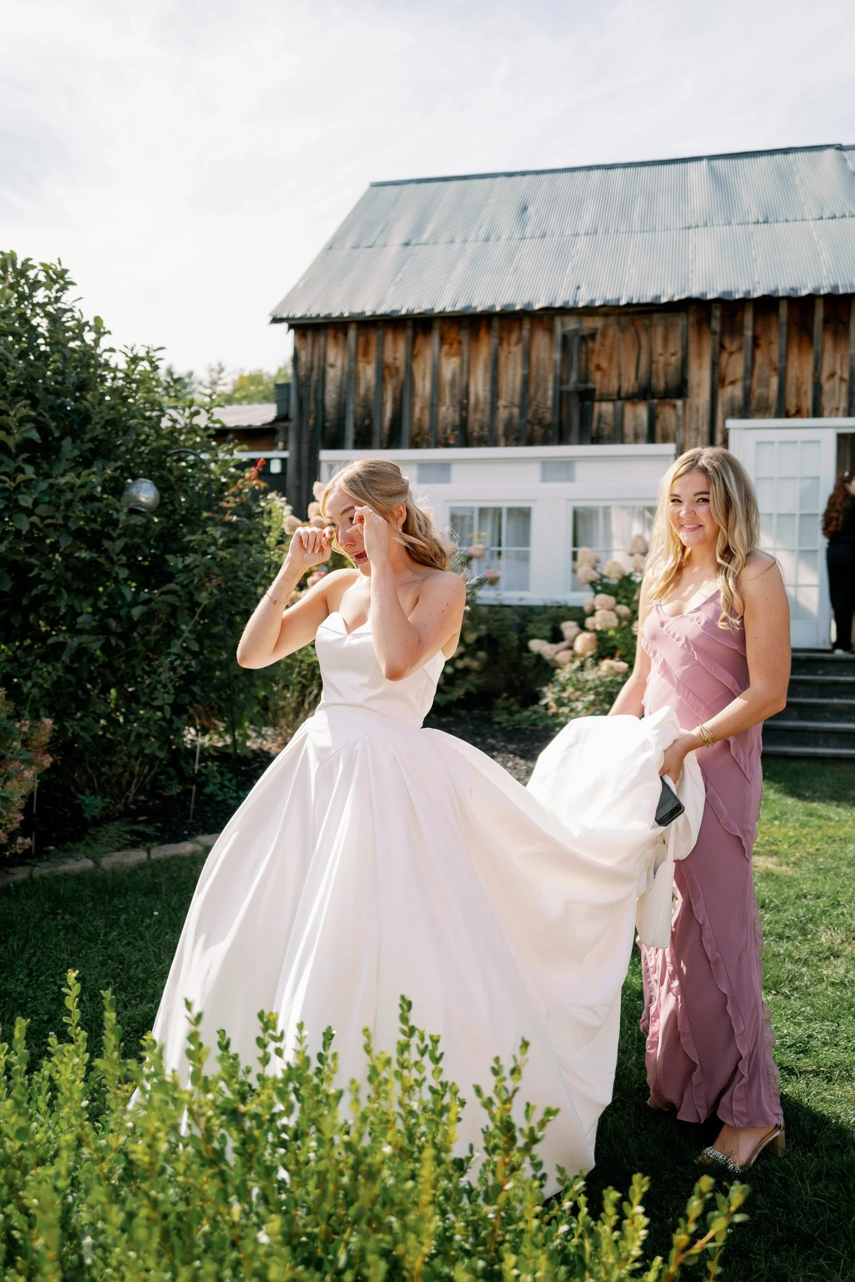 Someone holding the train of someone's wedding dress as they walk across a lawn 
