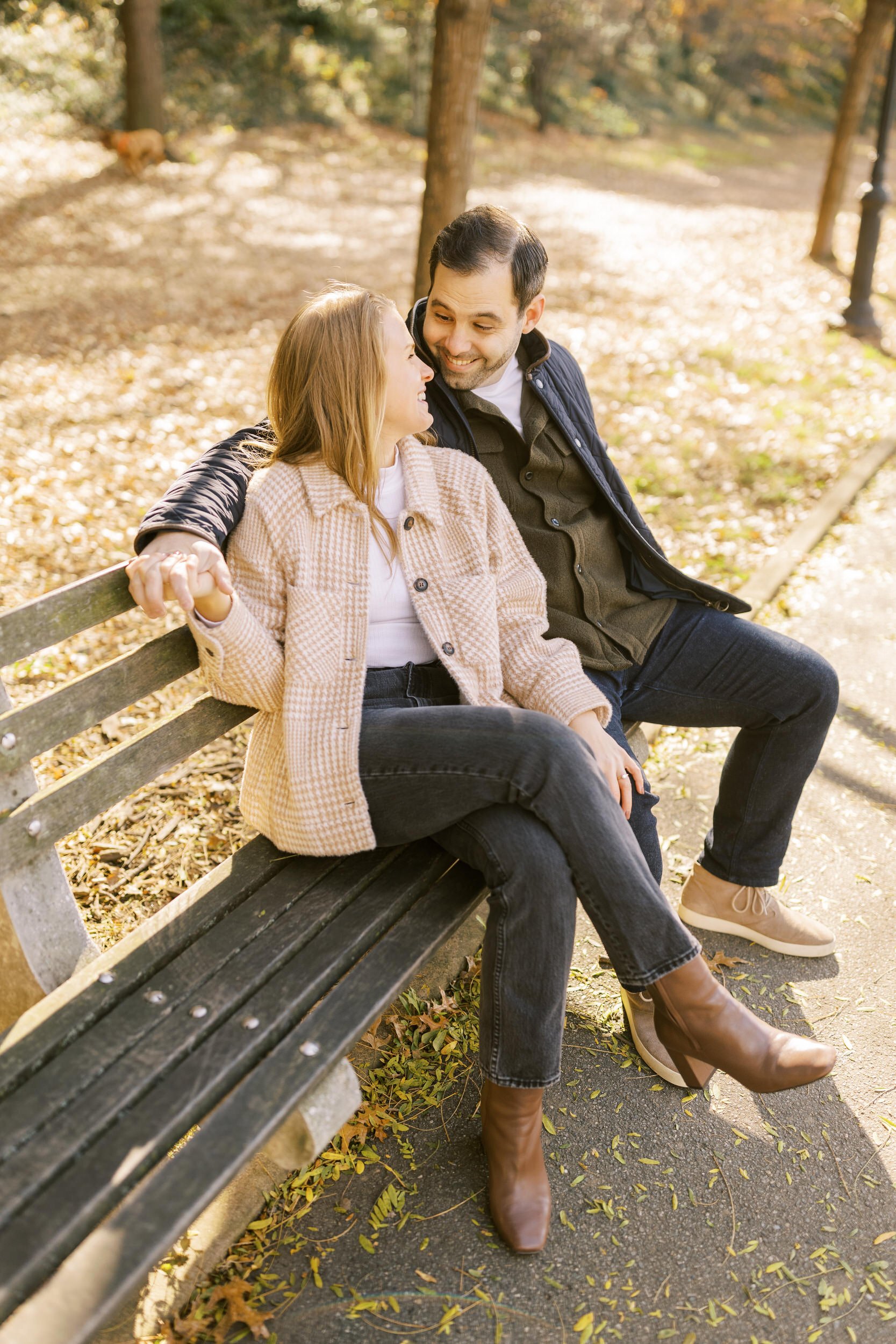 A couple sitting on a park bench smiling at each other 