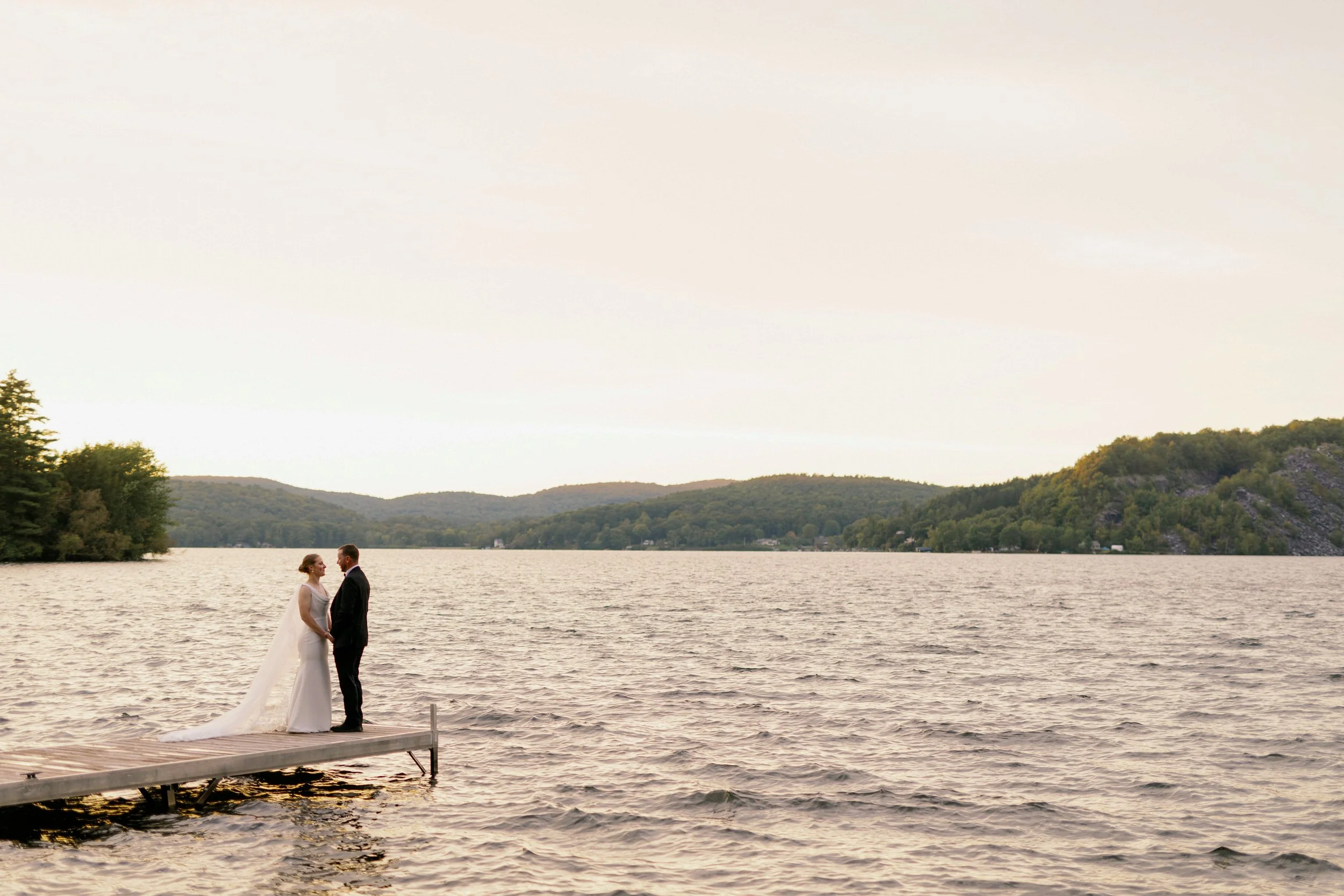 A newlywed couple standing on a small dock at sunset 