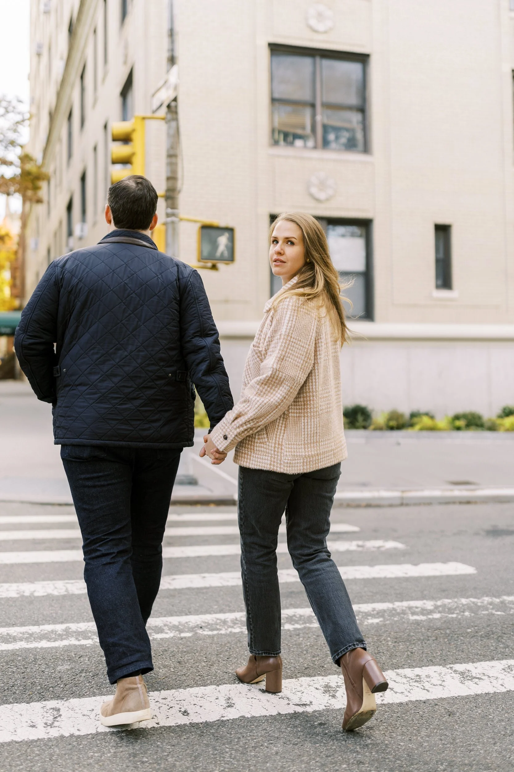 A couple holding hands and walking across a crosswalk as one looks back 