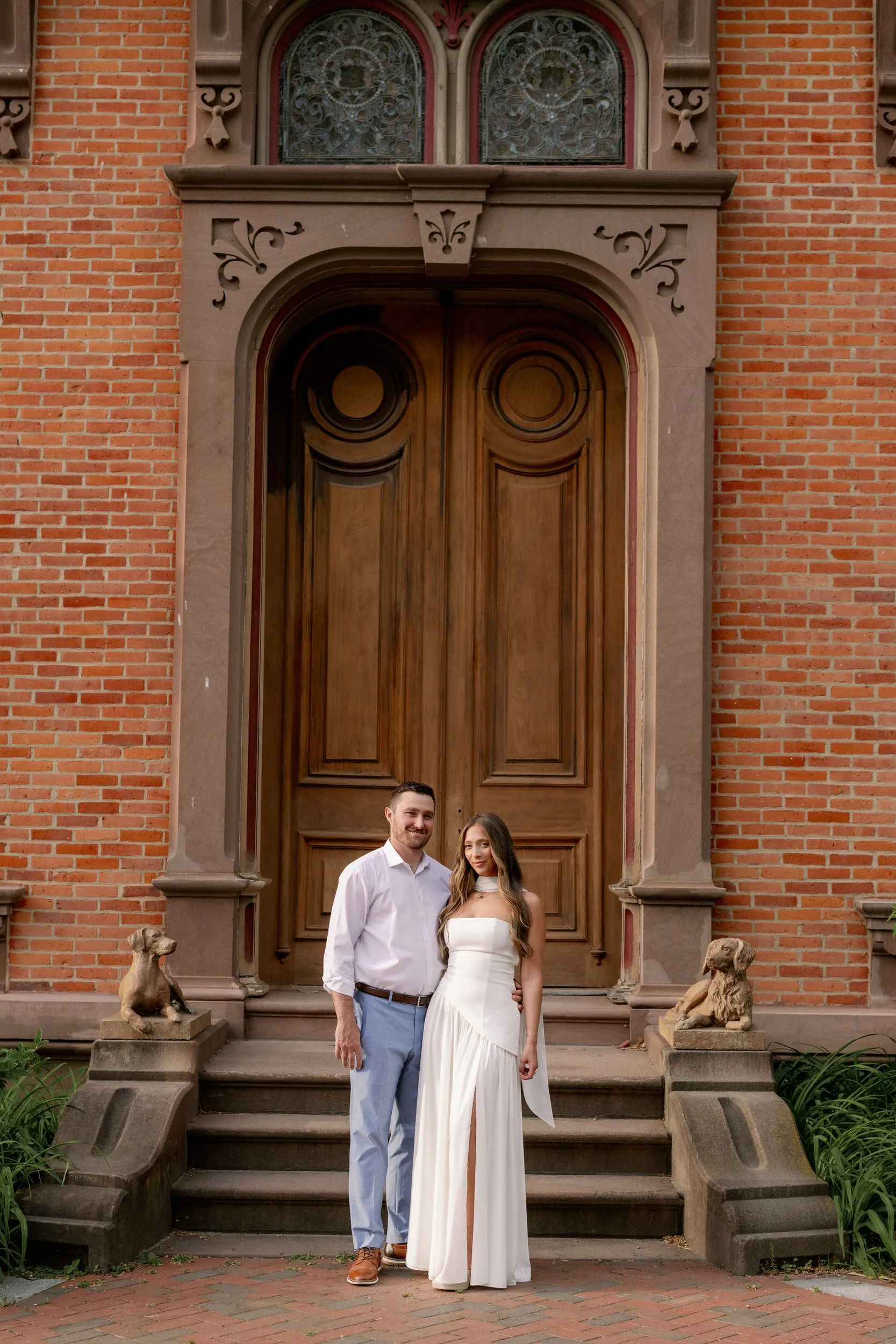 A couple smiling and standing in front of a red brick building 