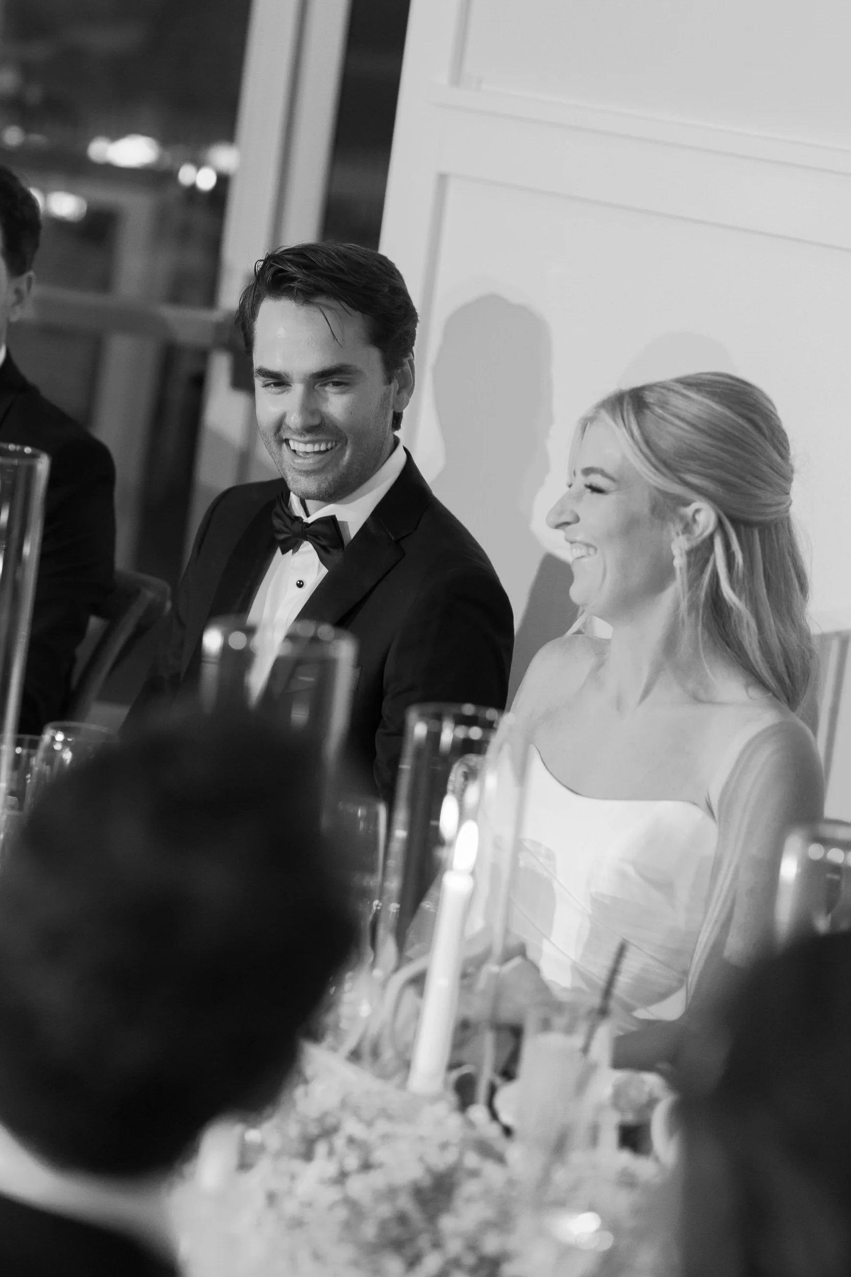 Newlyweds sitting at their reception laughing with their guests 