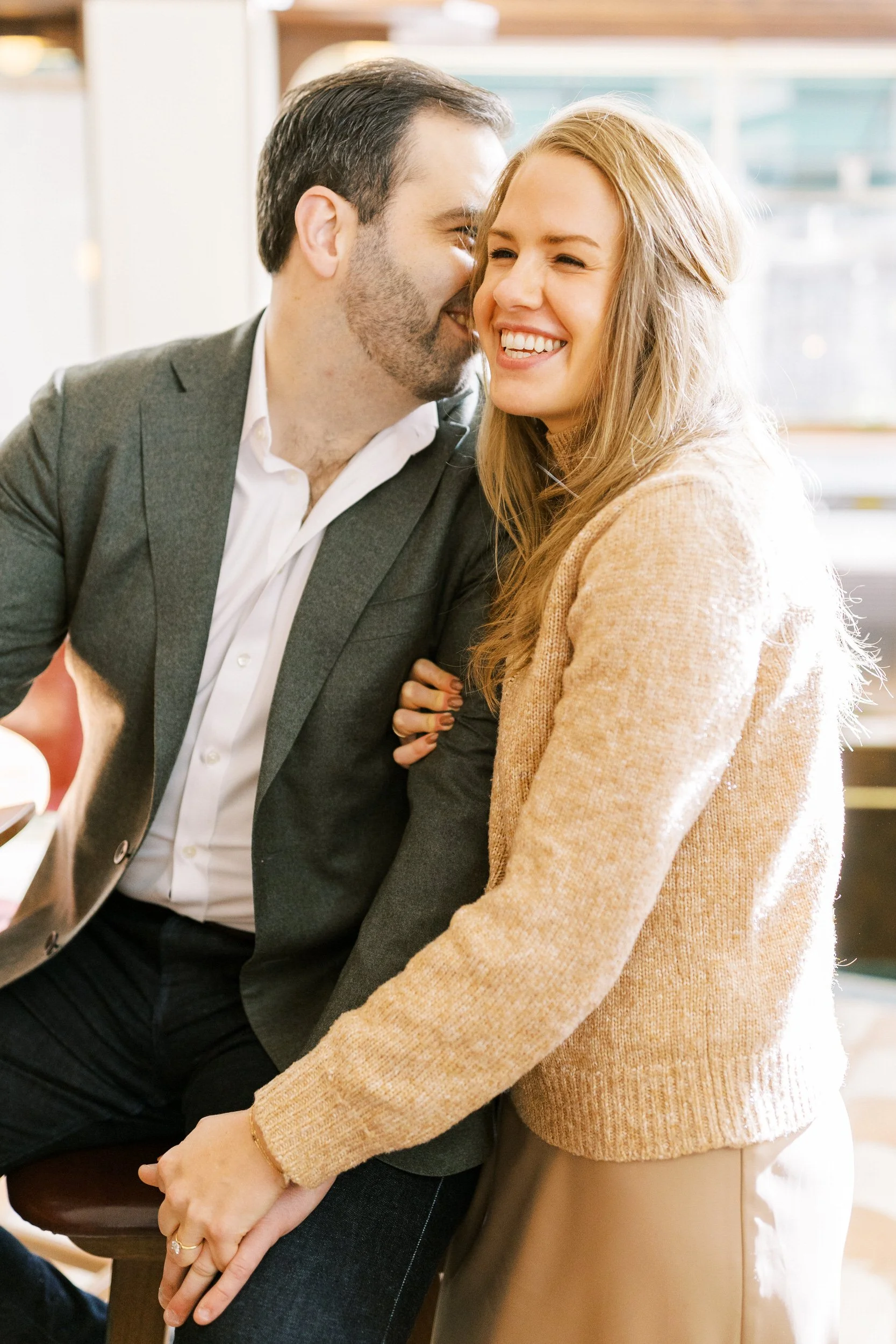 A person leaning in to their partner's ear as they both smile 