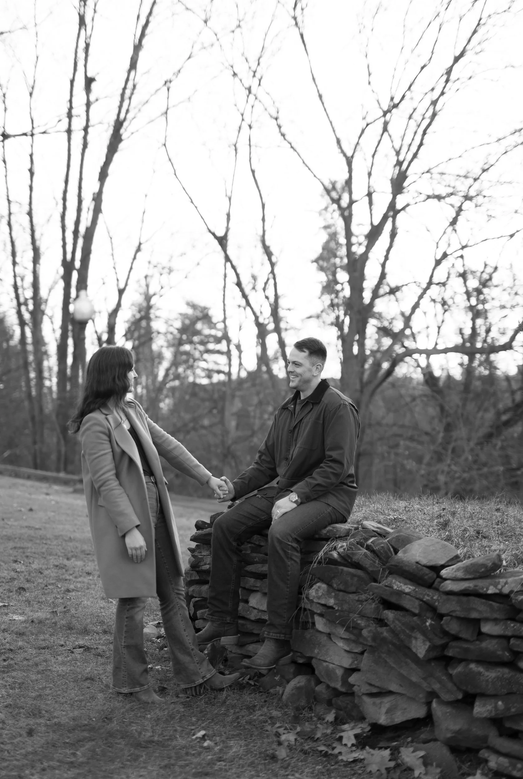 A person sitting on a stone wall with their partner in front of them 