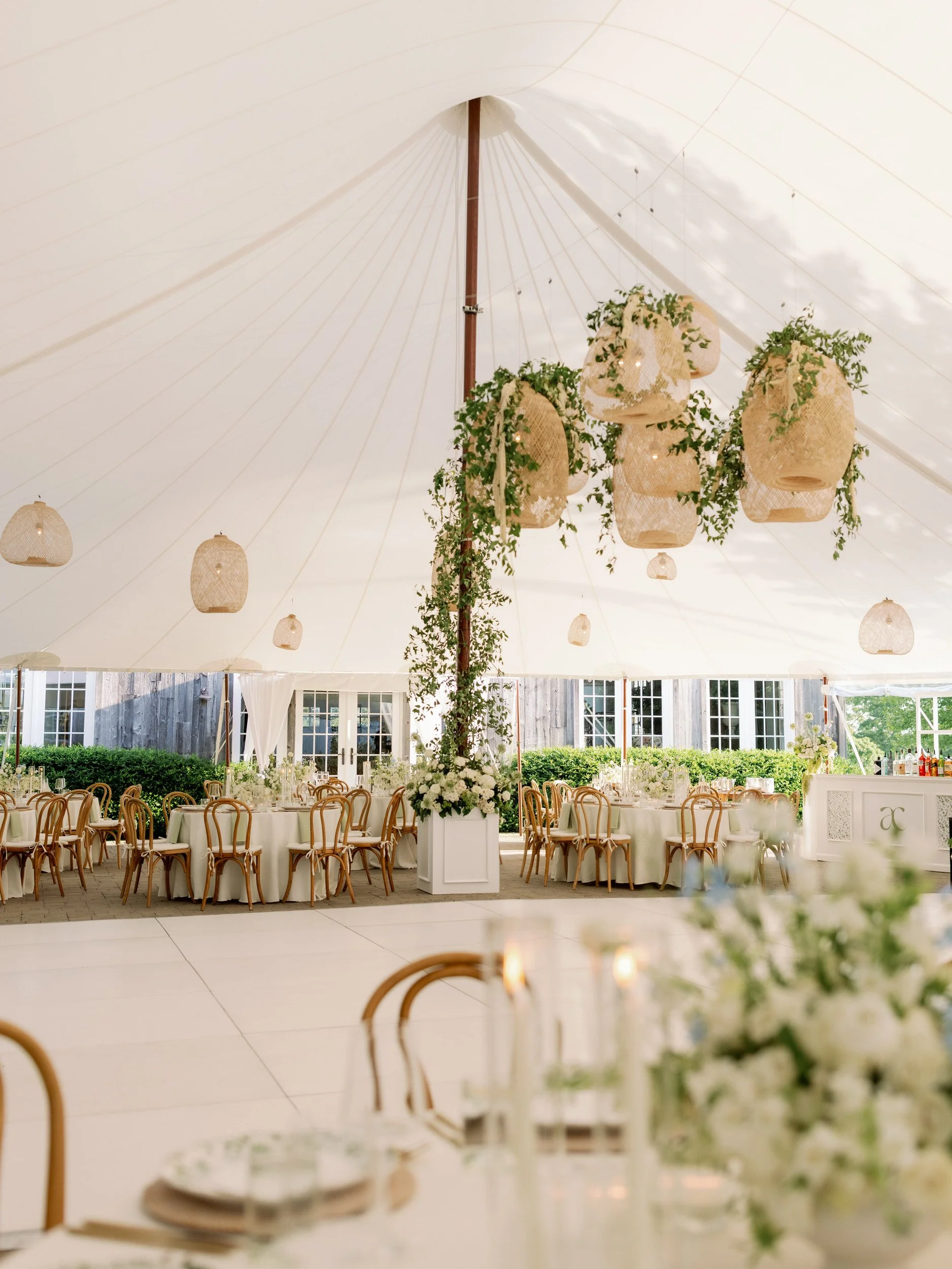 A large white tent with handing lanterns set up for a wedding reception 