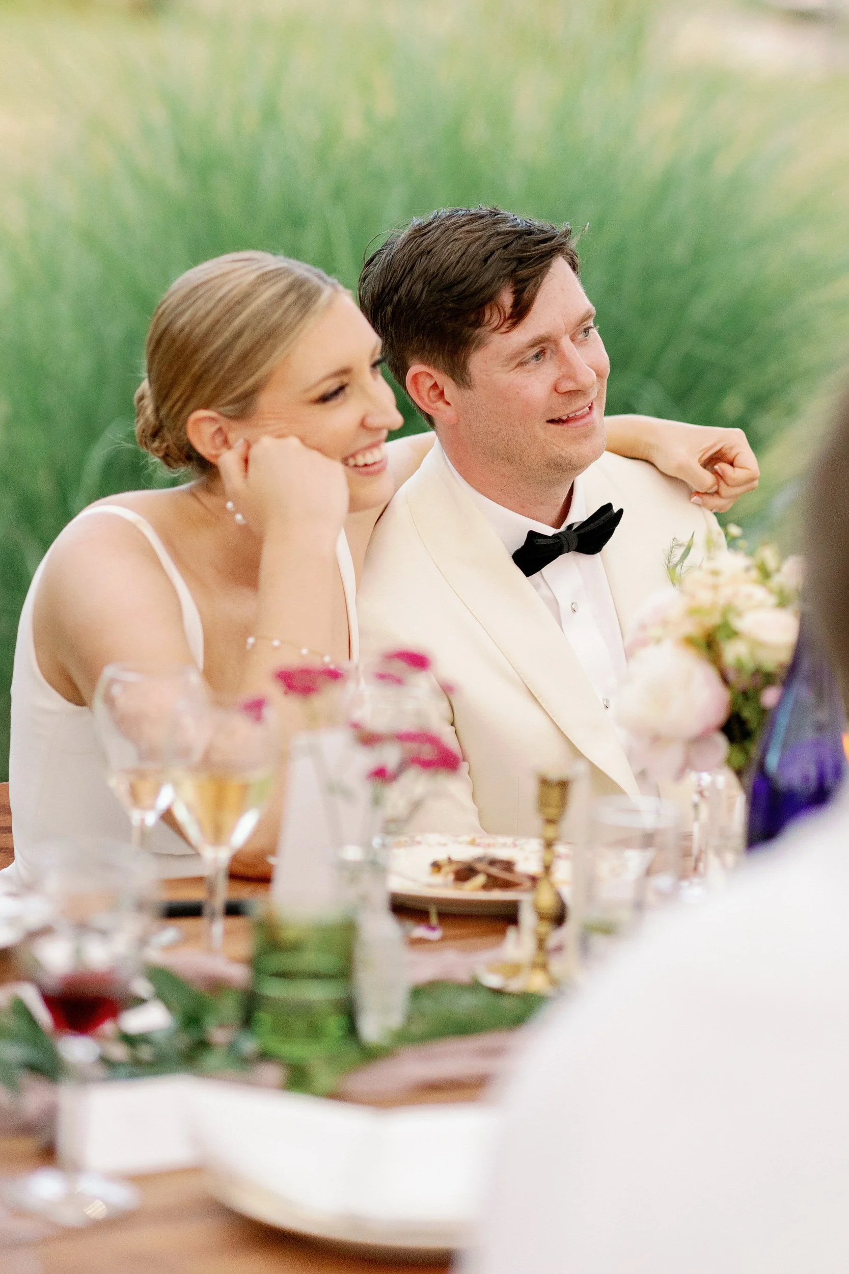 Newlyweds sitting close with their arms around each other during their wedding reception 