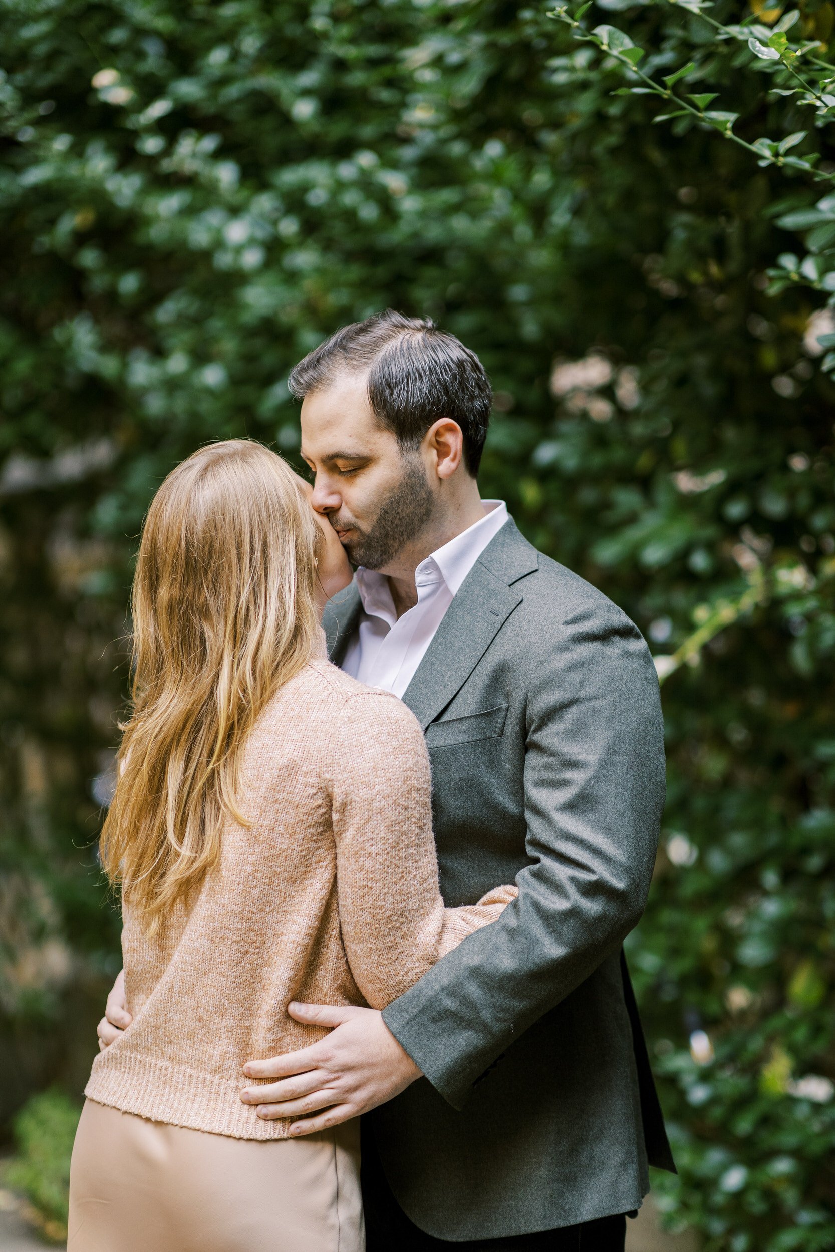 A couple kissing in a park with their arms around each other 