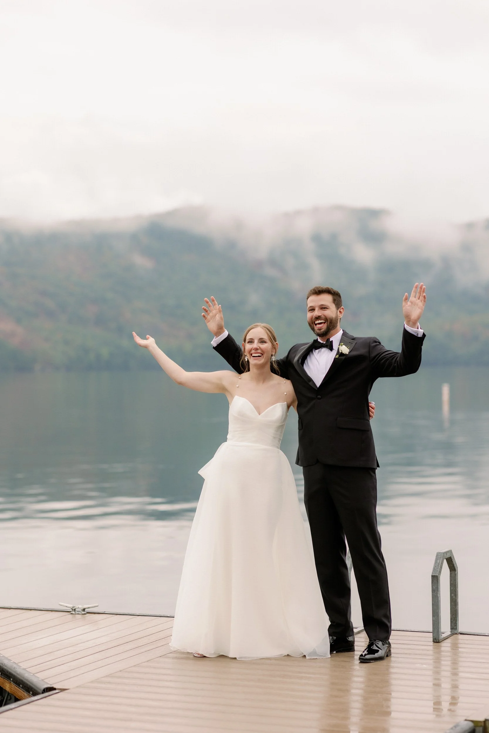 A newlywed couple standing on a dock with their arms outstretched