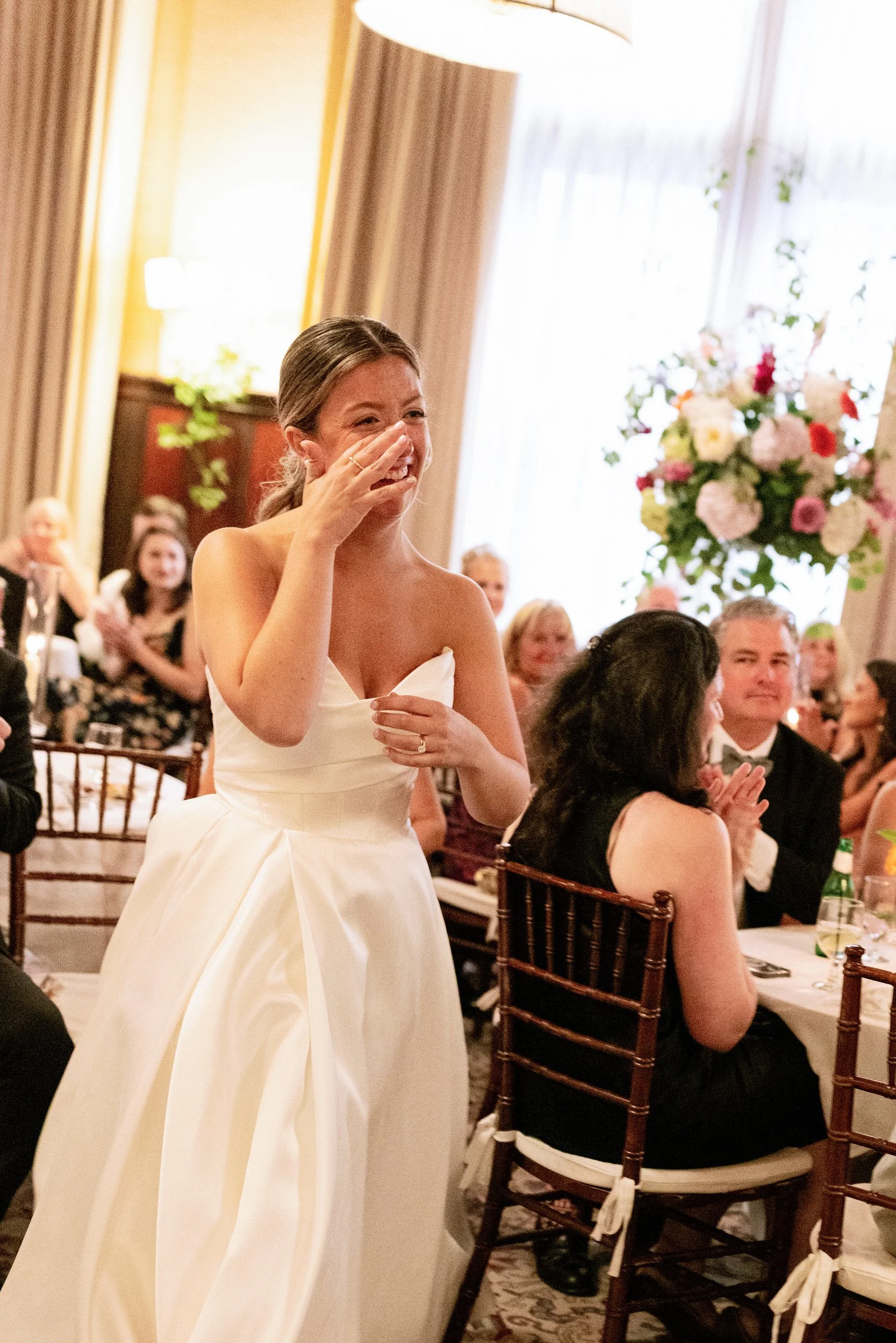 A newlywed in a wedding dress wiping a tear away at their wedding reception 