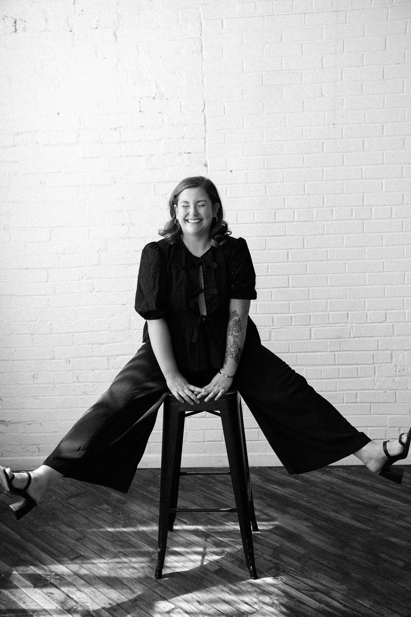 Maisie sitting on a stool laughing as her feet are kicked out to the side