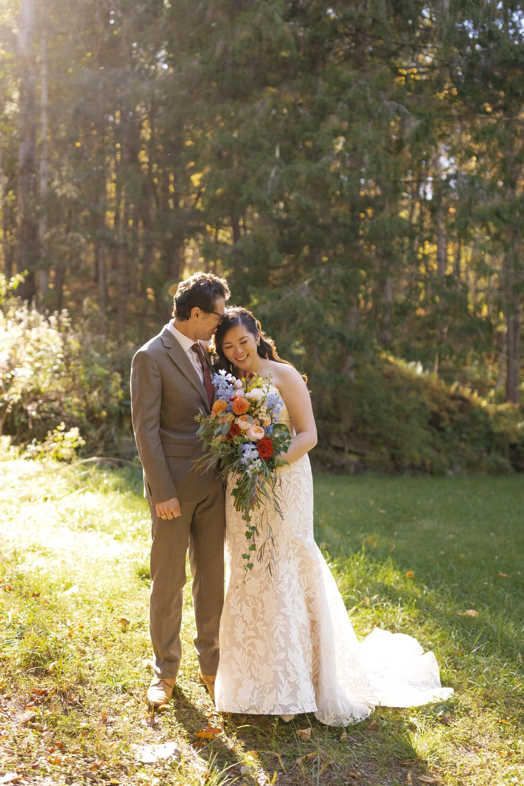 A newlywed leaning into their partner as they stand on the edge of a wooded area