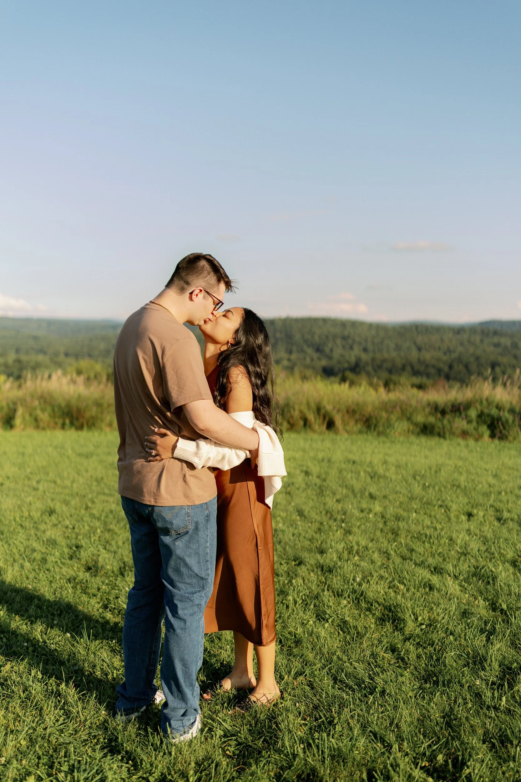 A couple with their arms around each other kissing in a field 