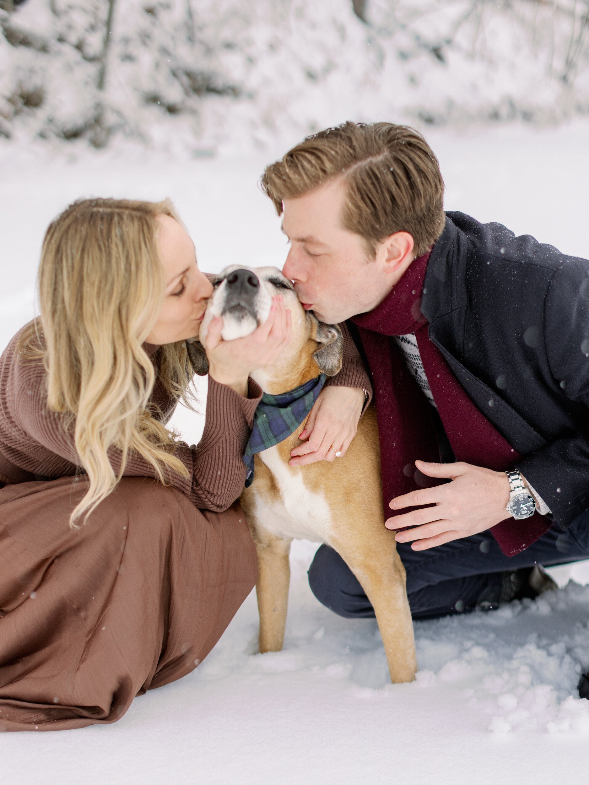 A couple sitting on either side of a dog kissing its head