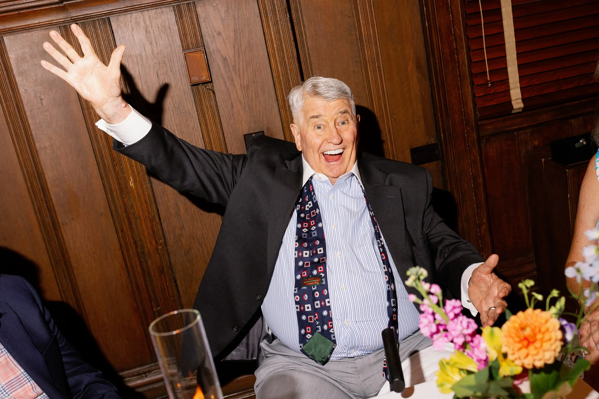 A wedding guests with an untied tie with their hands outstretched and a big smile on their face
