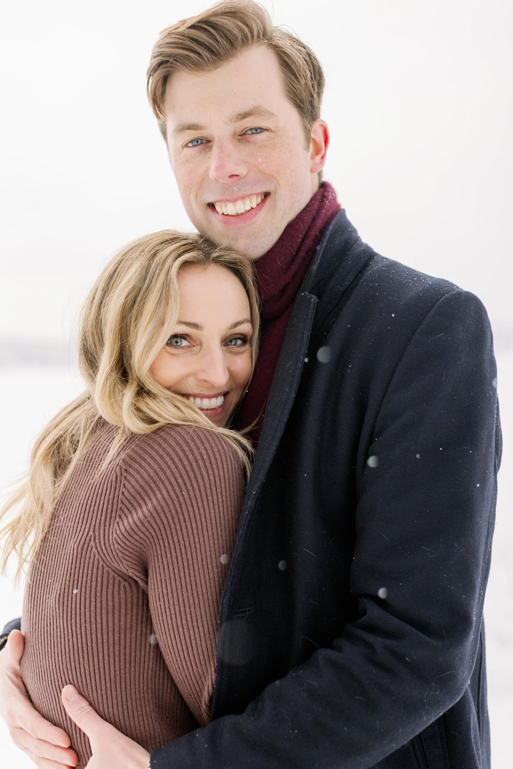 A couple hugging closely as it snows 