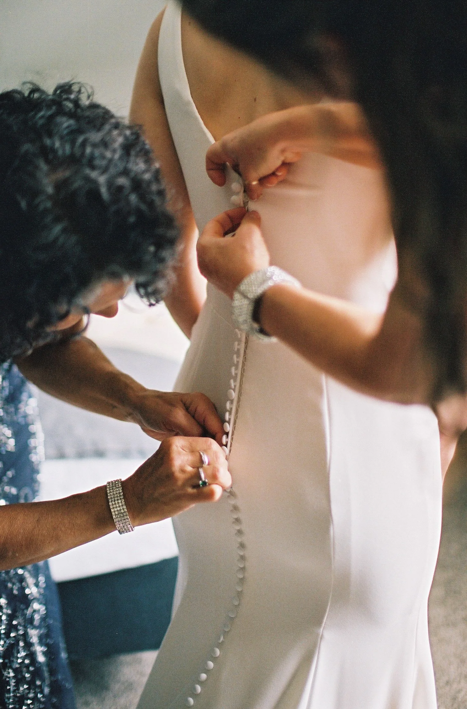 Two people helping someone button up their wedding dress 
