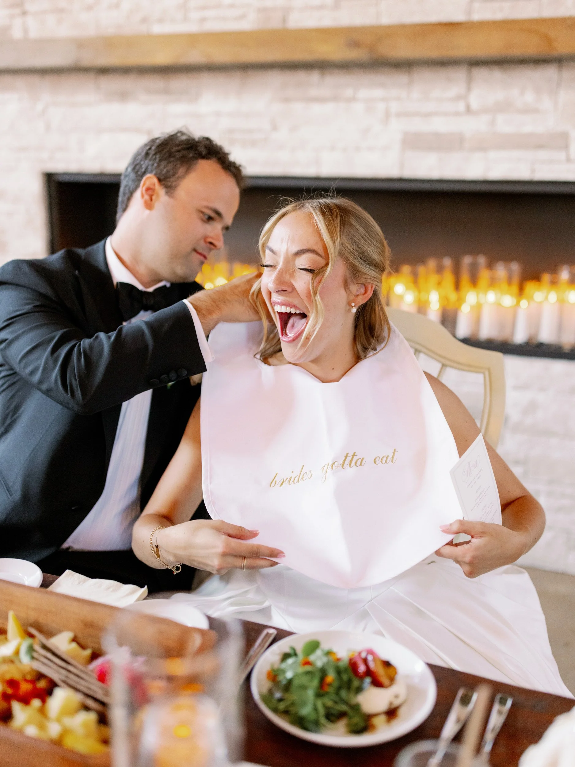 A newlywed laughing as their partner puts a bib on them