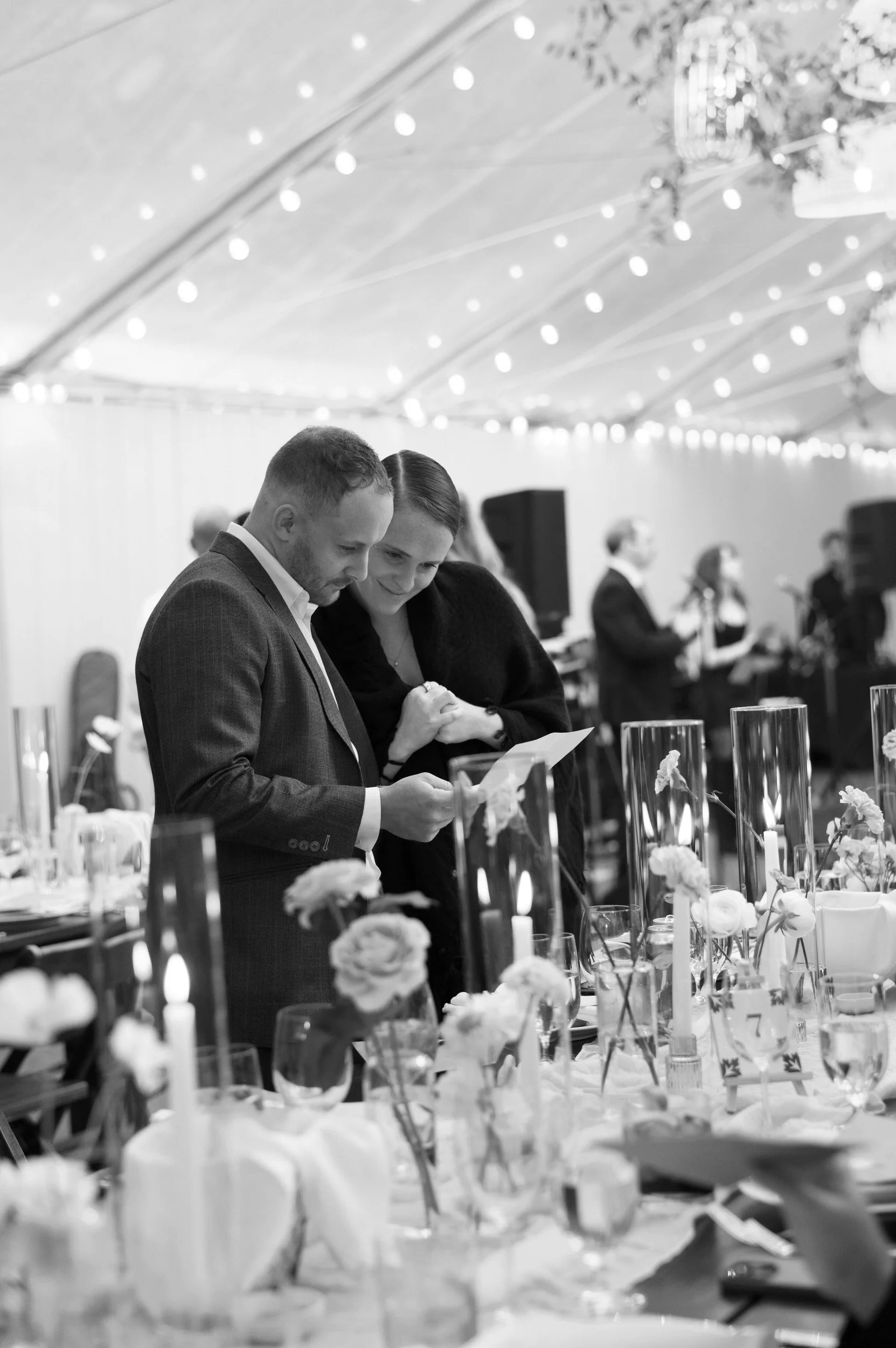 Wedding guests reading a note while standing next to a table at a reception 