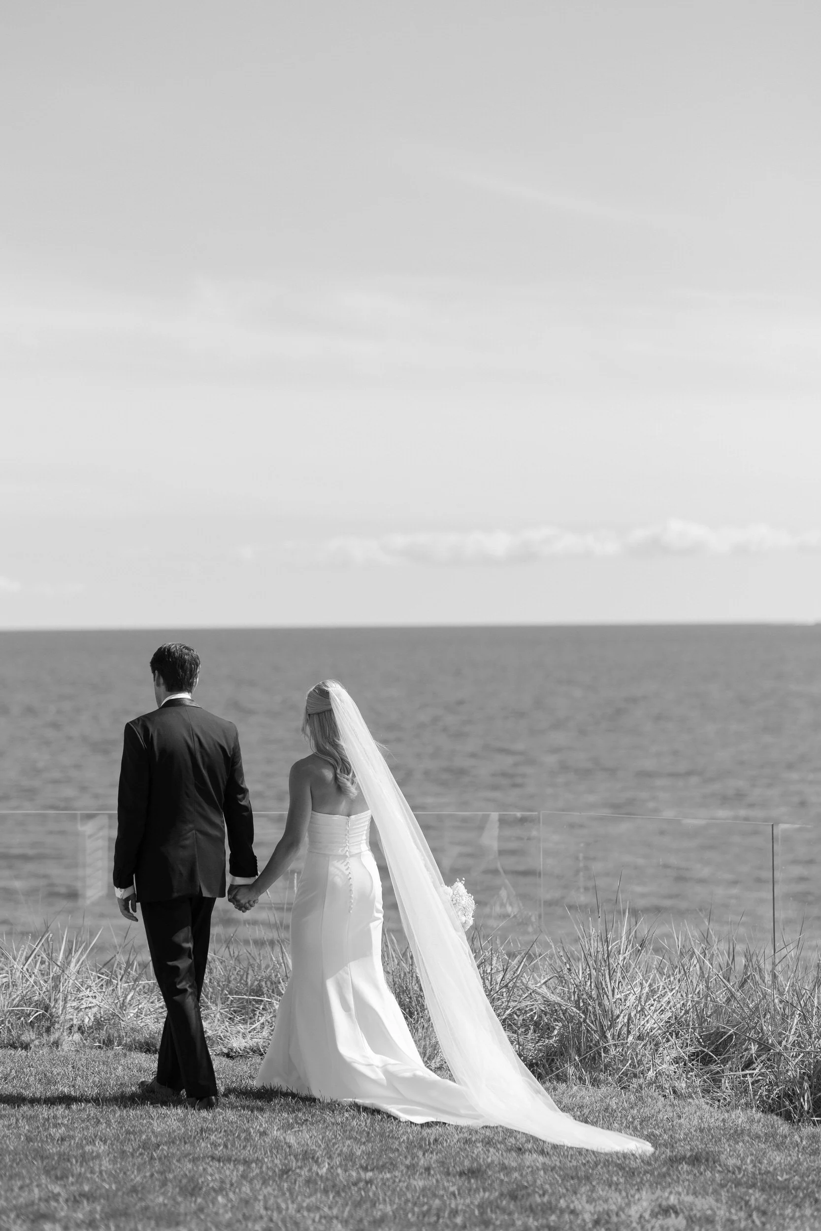 Newlyweds holding hands and walking along the grassy bank of the water