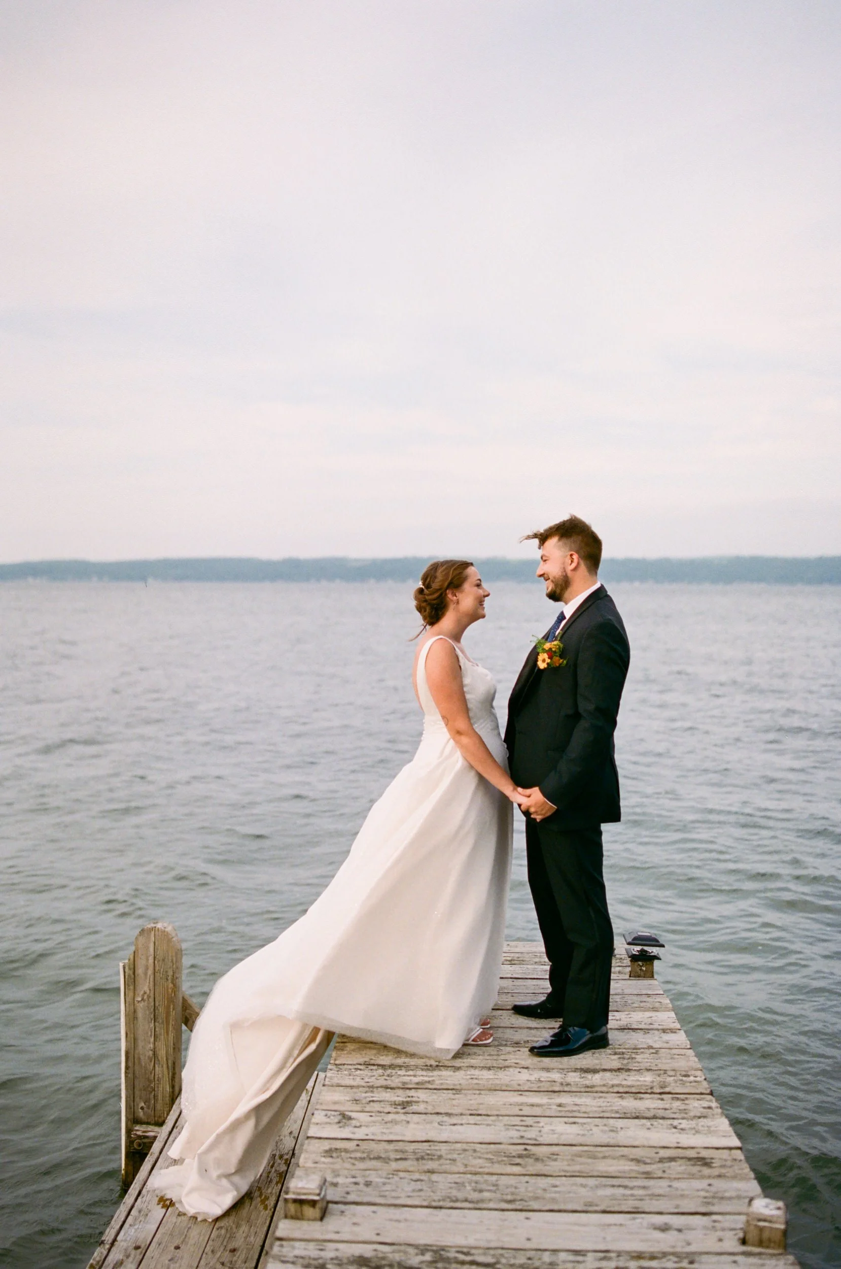 Newlyweds holding hands and standing on a small wooden dock 