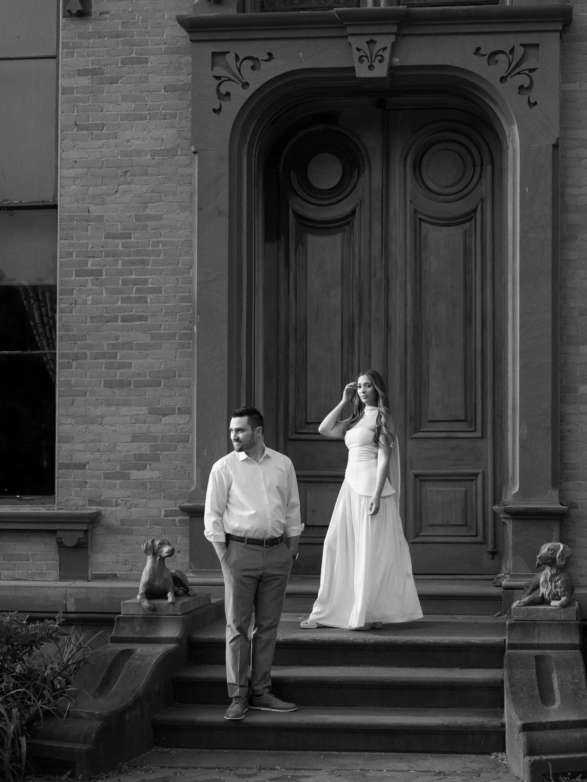 A couple standing on the steps to a brick building looking off to the side 