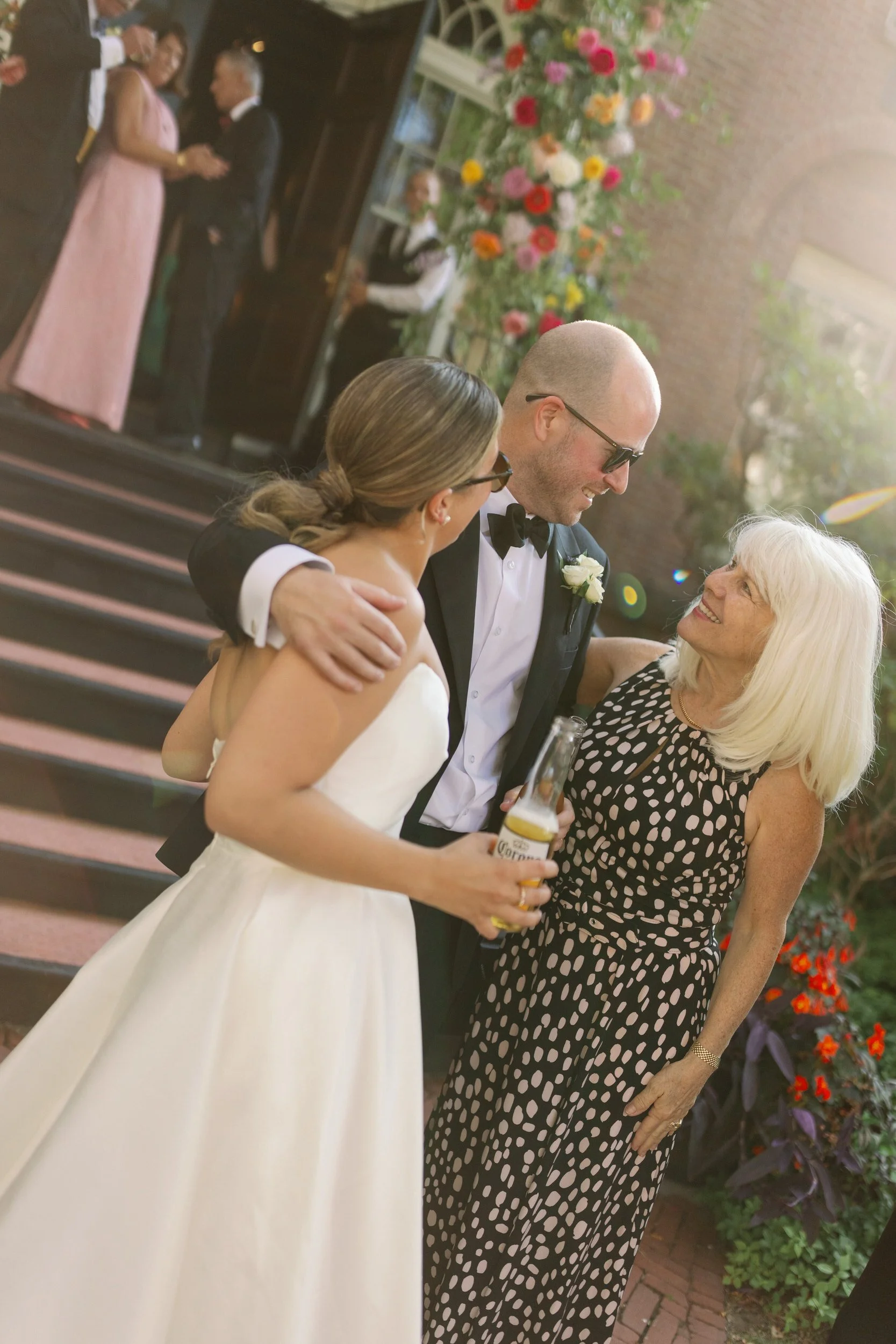 Newlyweds with their arms around each other as they smile at a wedding guest